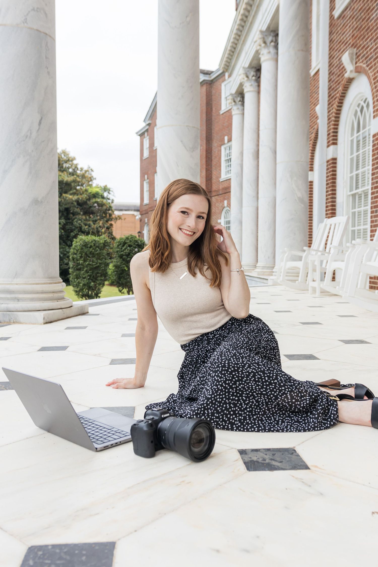 Photographer Sarah Frady sitting on the marble ground with her camera and computer smiling.