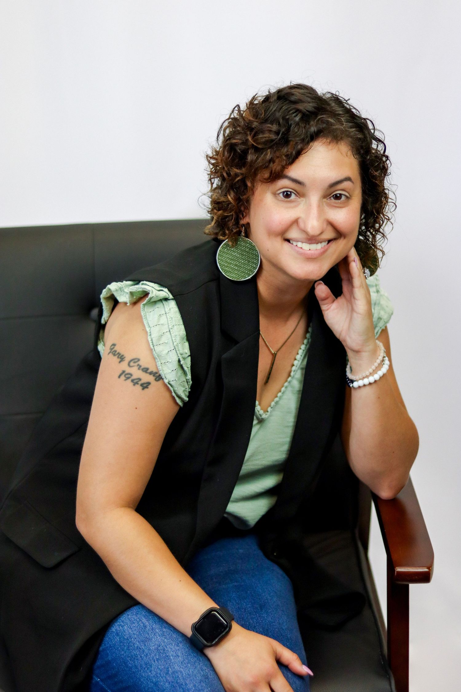 Realtor in a chair posing and smiling with her hand on her chin and elbow on the arm rest.