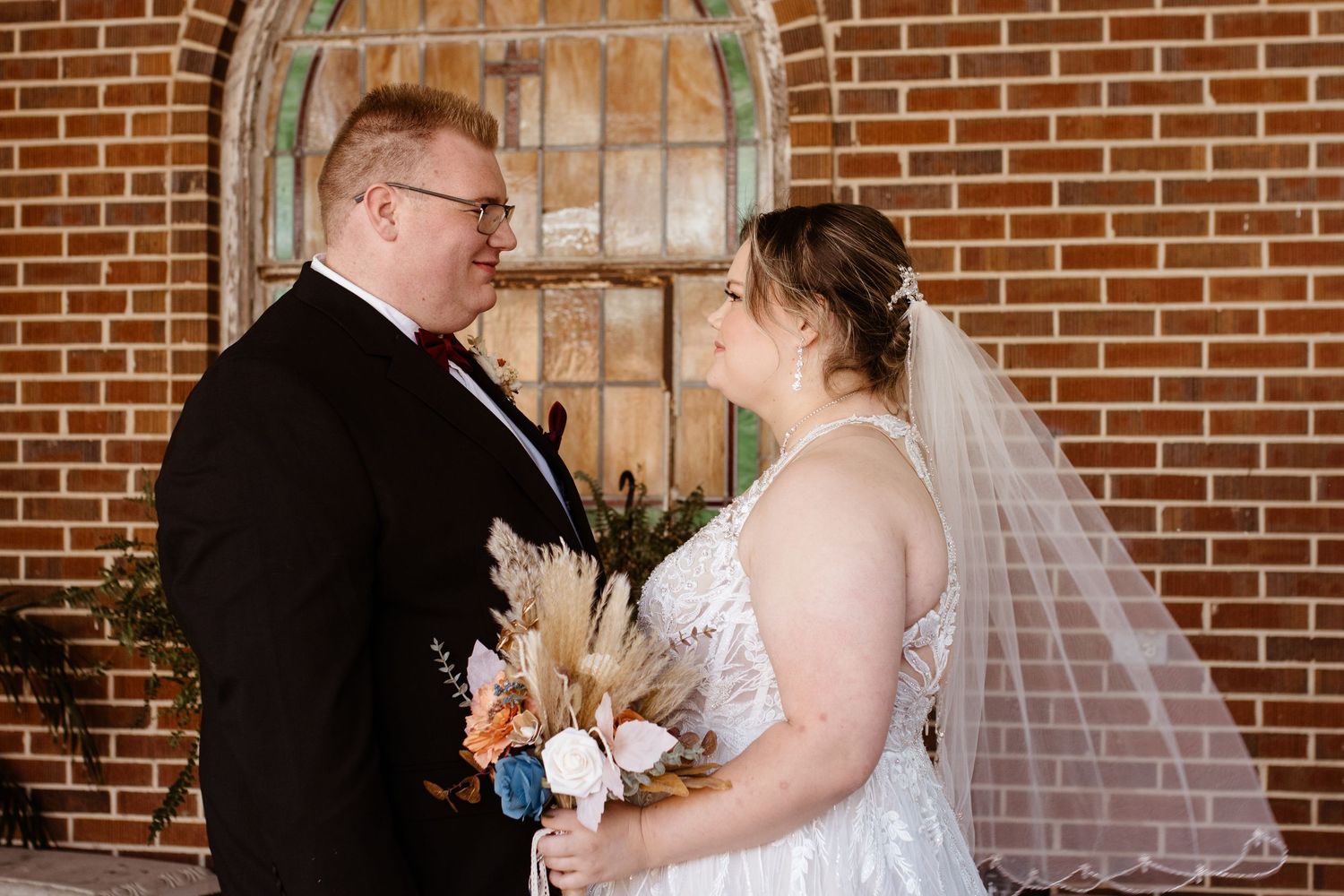 Couple on their wedding day facing each other. Bouquet in bride's hand.