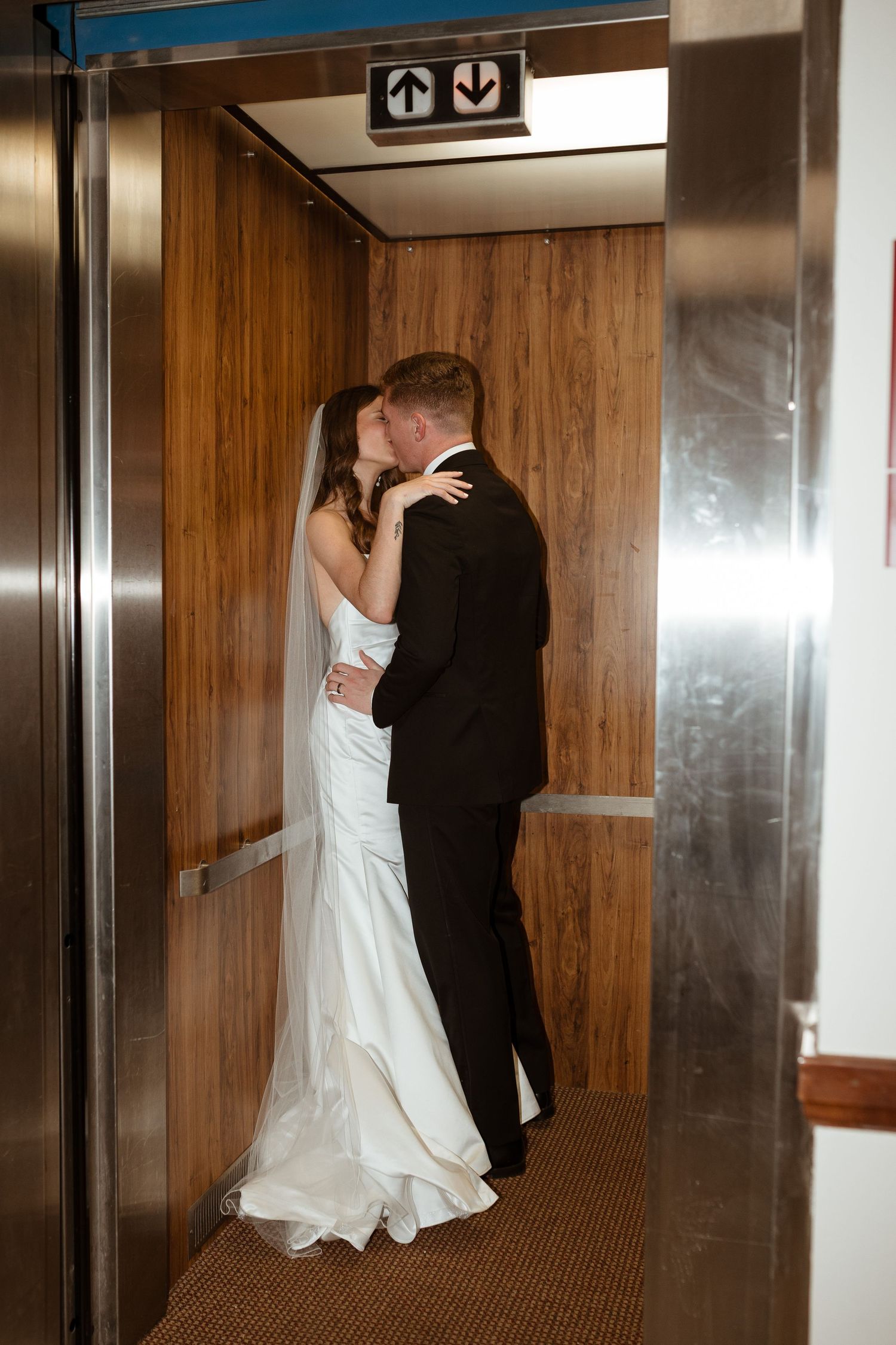 Bride and groom kissing in an elevator on their wedding day.