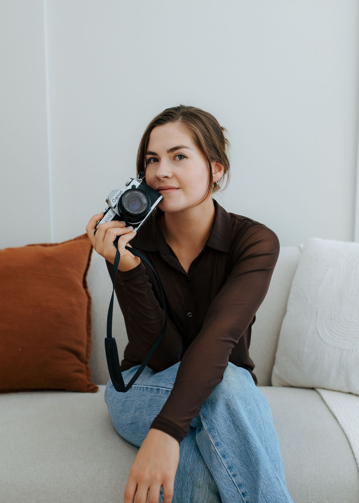 Young woman sitting on couch holding vintage film camera, looking away.