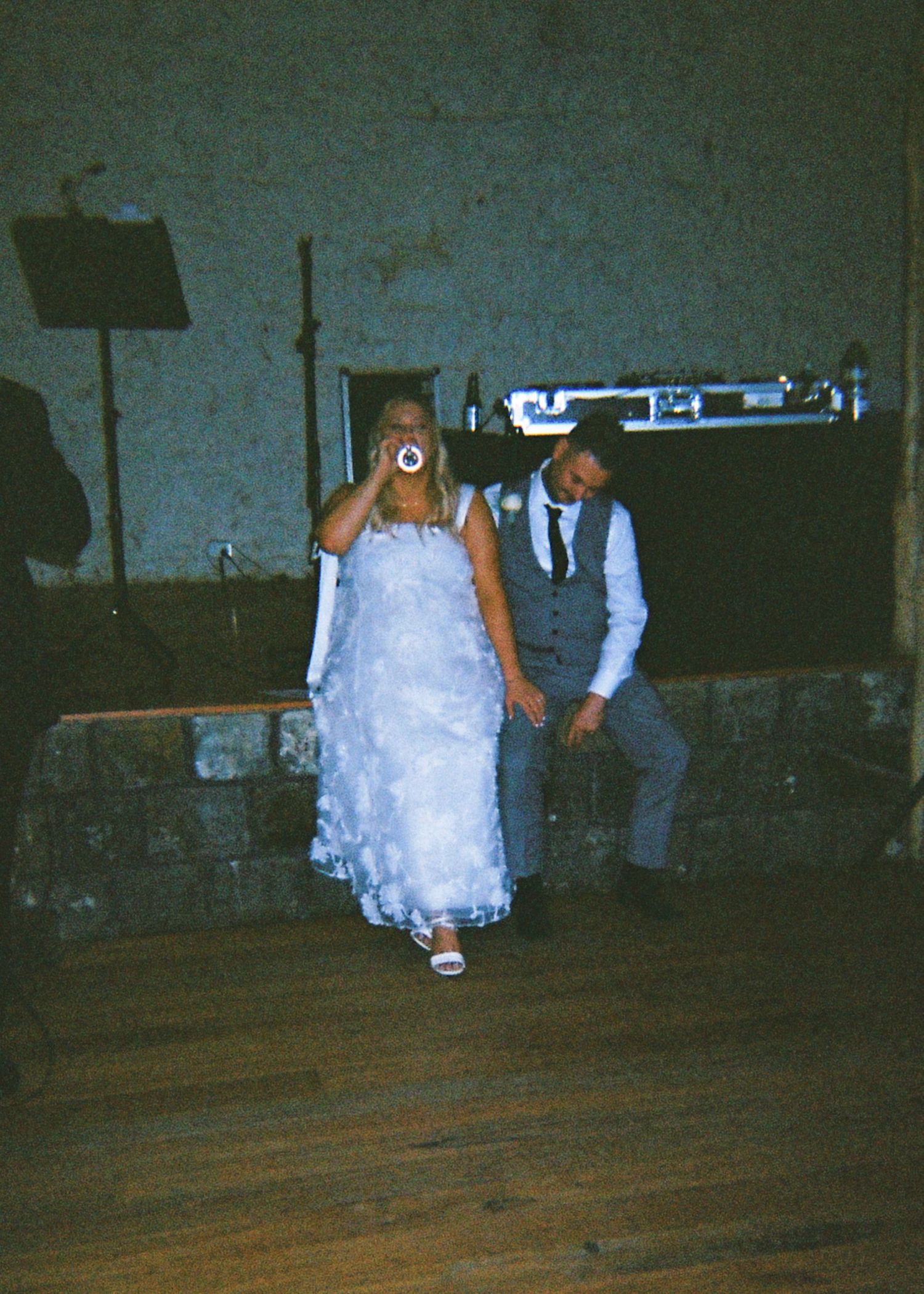 Bride in white gown and groom in grey vest dancing together at their wedding reception.