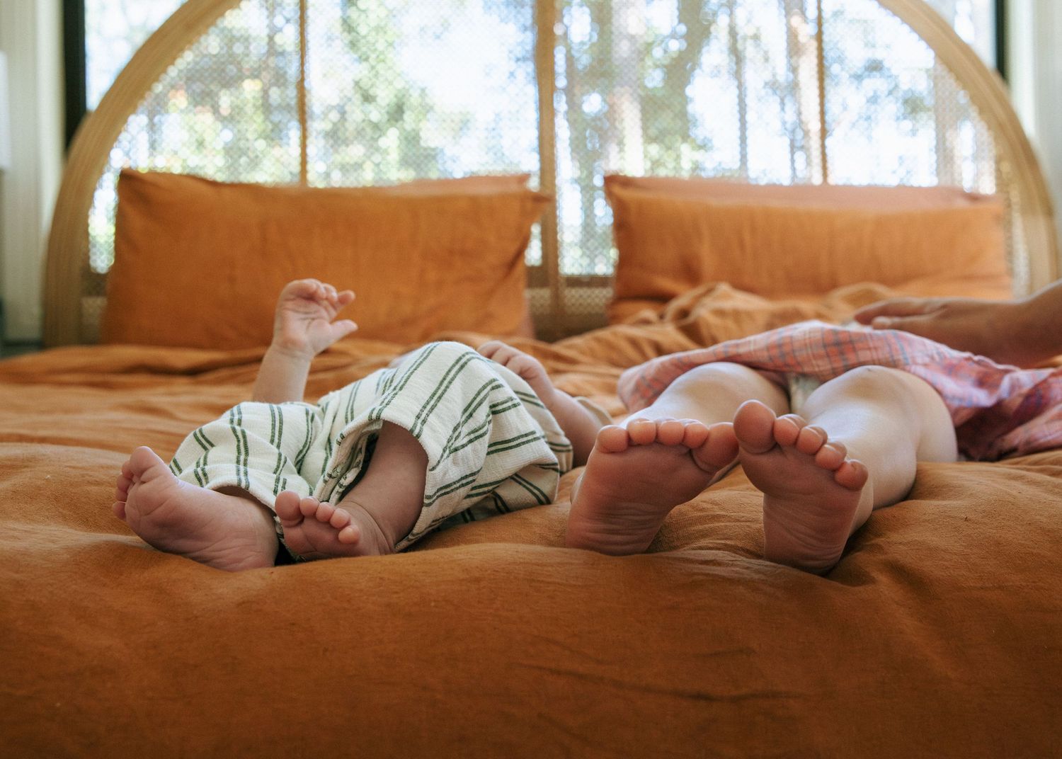 Newborn baby and toddler lying side by side on an orange bed near a window.