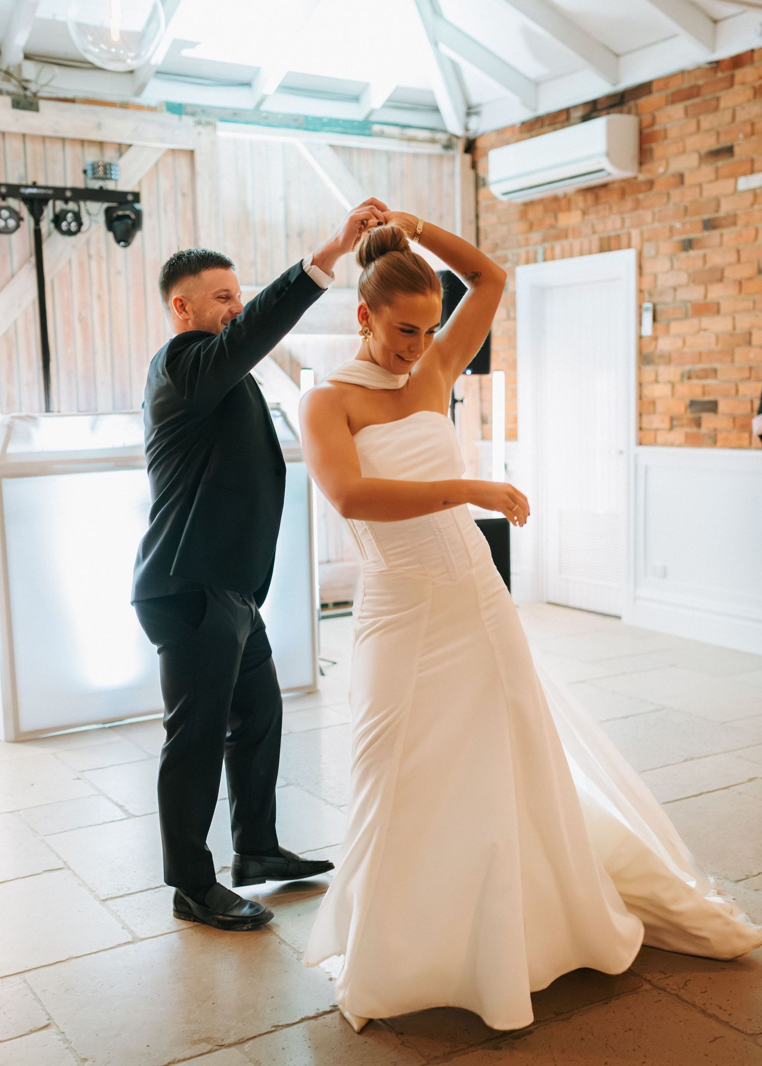 Groom spinning bride in white halter gown during first dance at wedding reception.