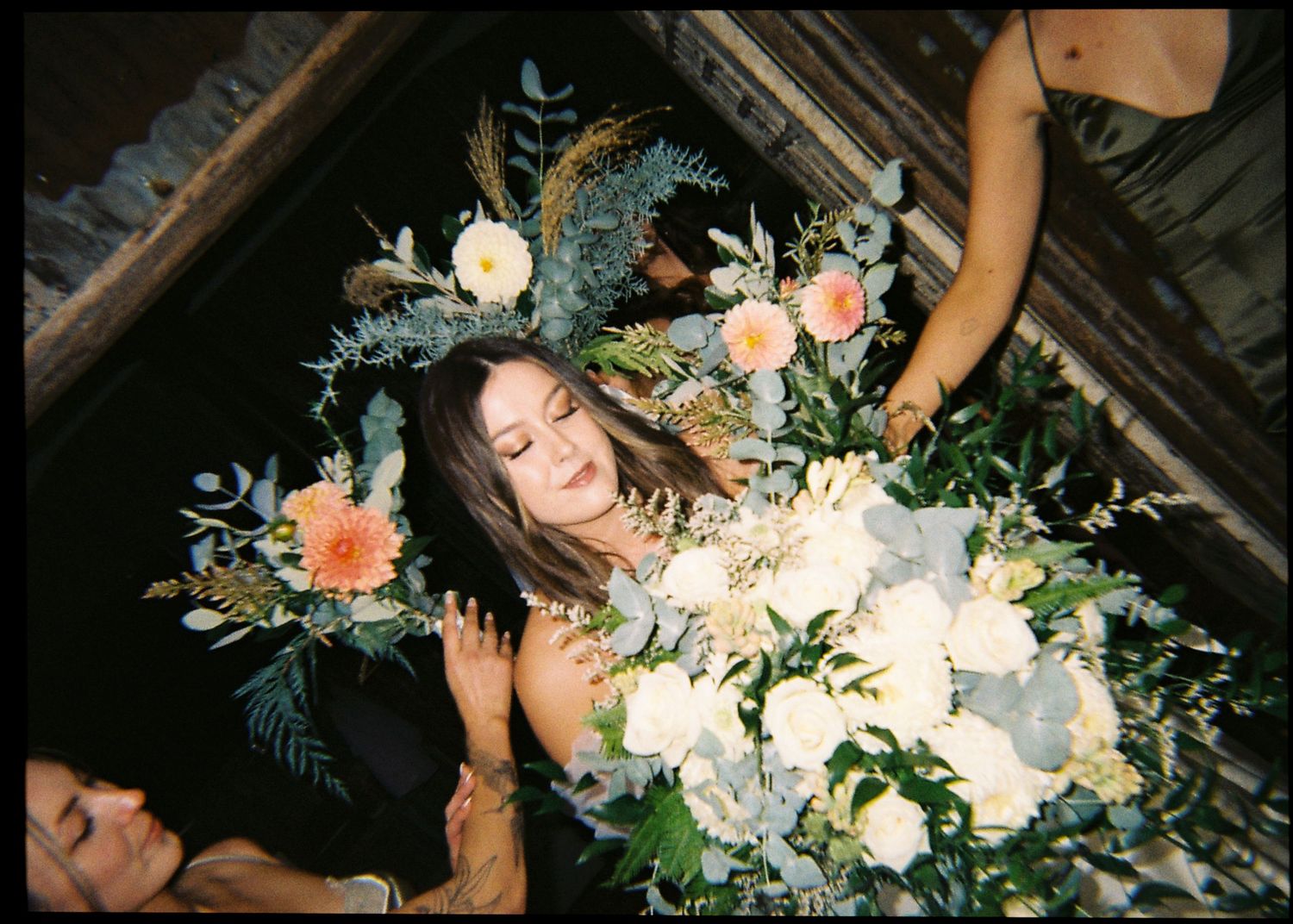 Bride lying in floral bath surrounded by lush blooms and greenery in a romantic wedding ritual.
