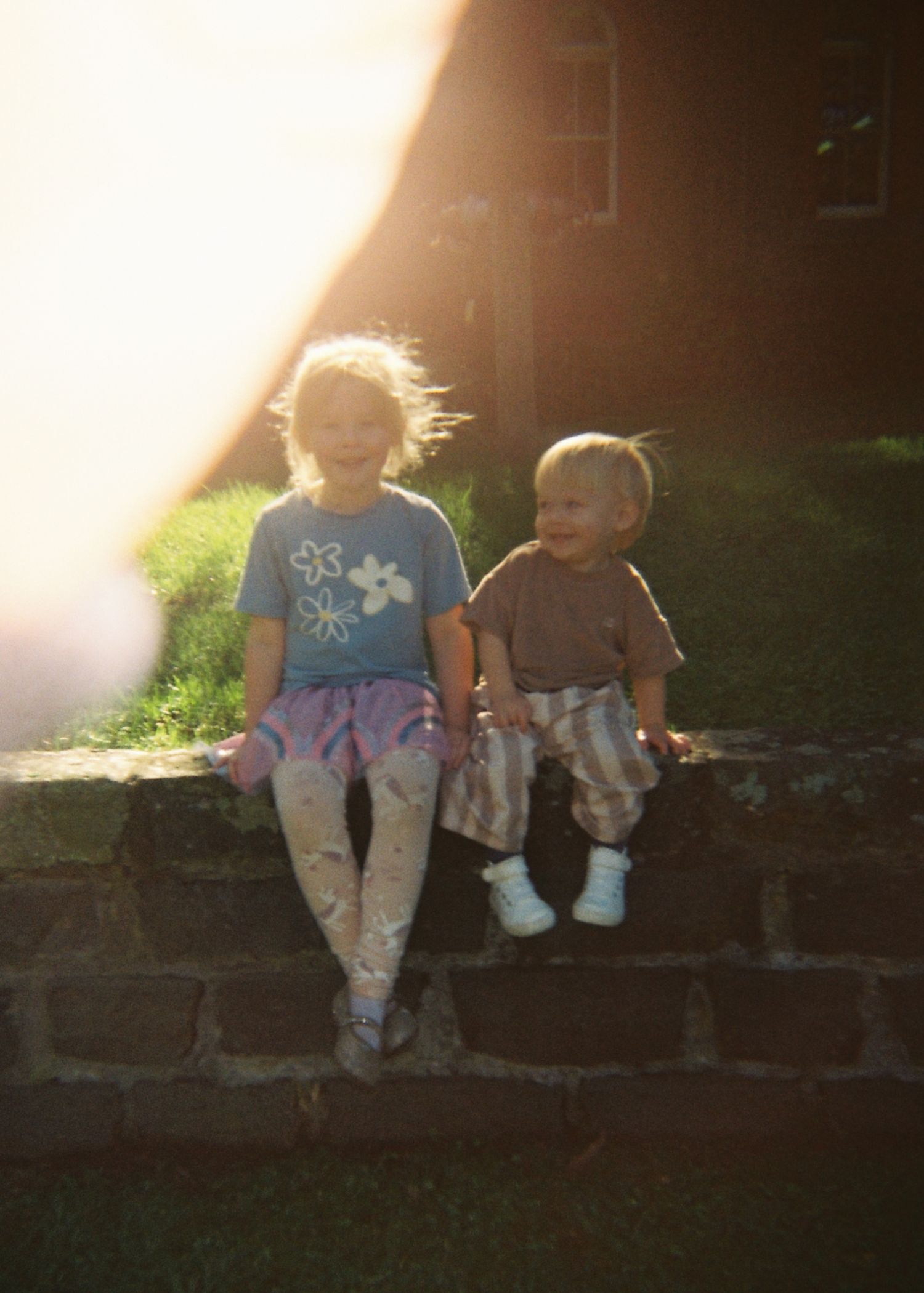 Two young children sit together on stone steps bathed in warm golden sunset light.