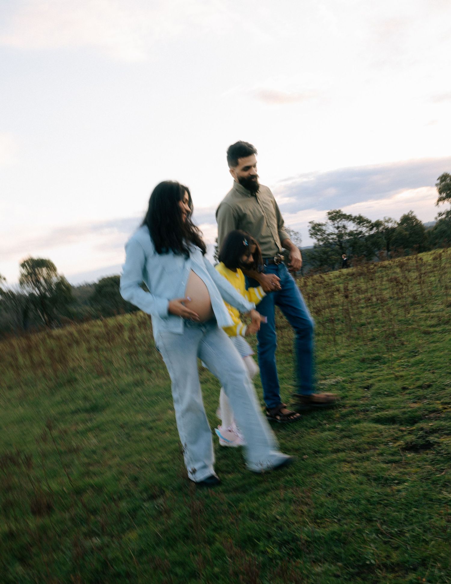 Pregnant woman and family enjoy golden hour maternity shoot in lush meadow.