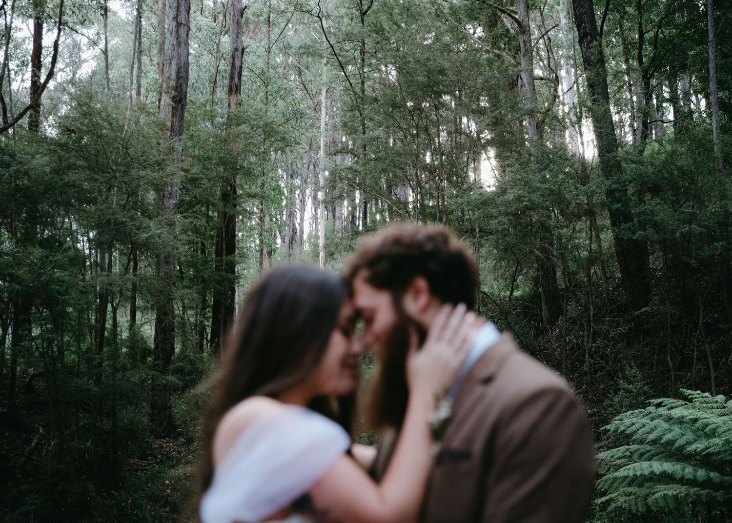 Couple sharing a romantic kiss in a lush green forest during their wedding day photoshoot.