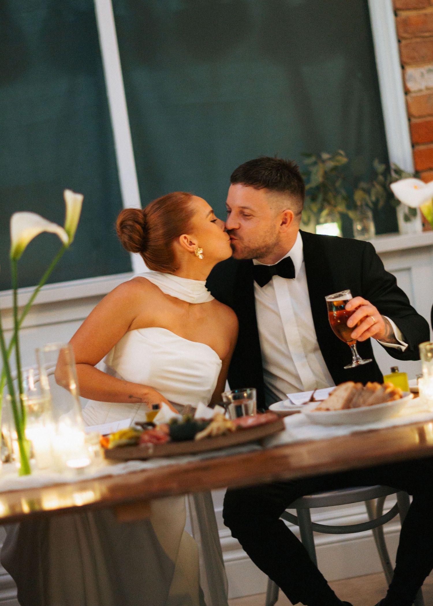 Bride and groom sharing a kiss at wedding reception dinner table with calla lily centerpieces.