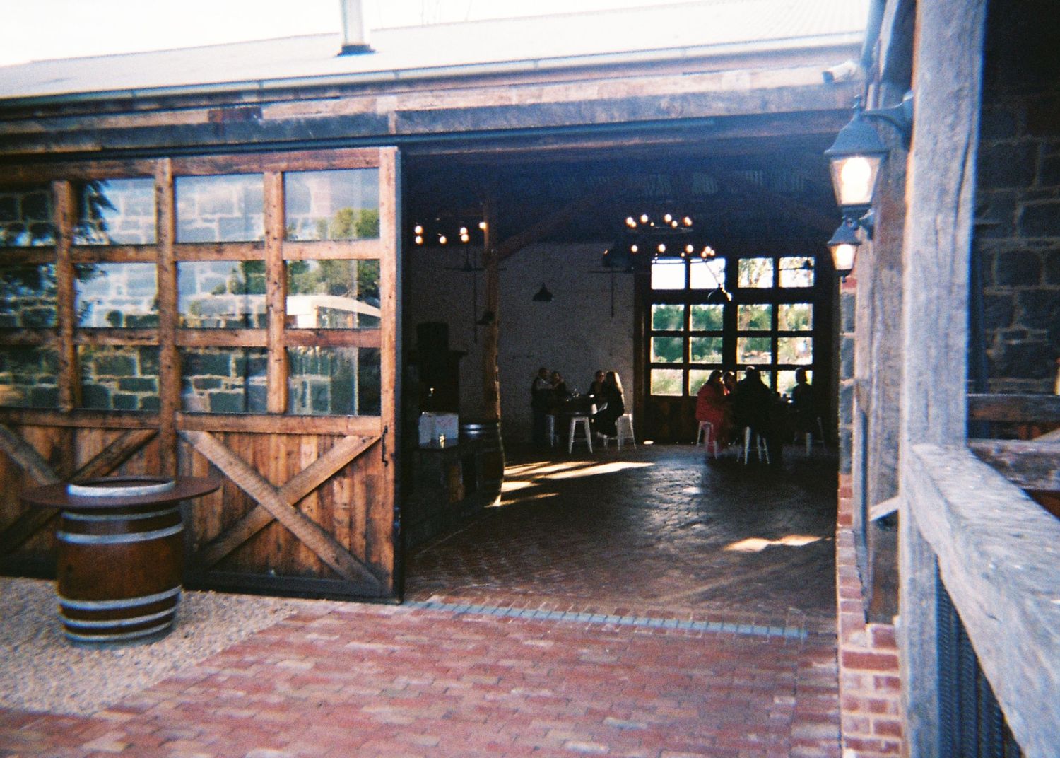 Rustic barn wedding venue entrance with wooden doors, brick flooring, and barrel decoration.