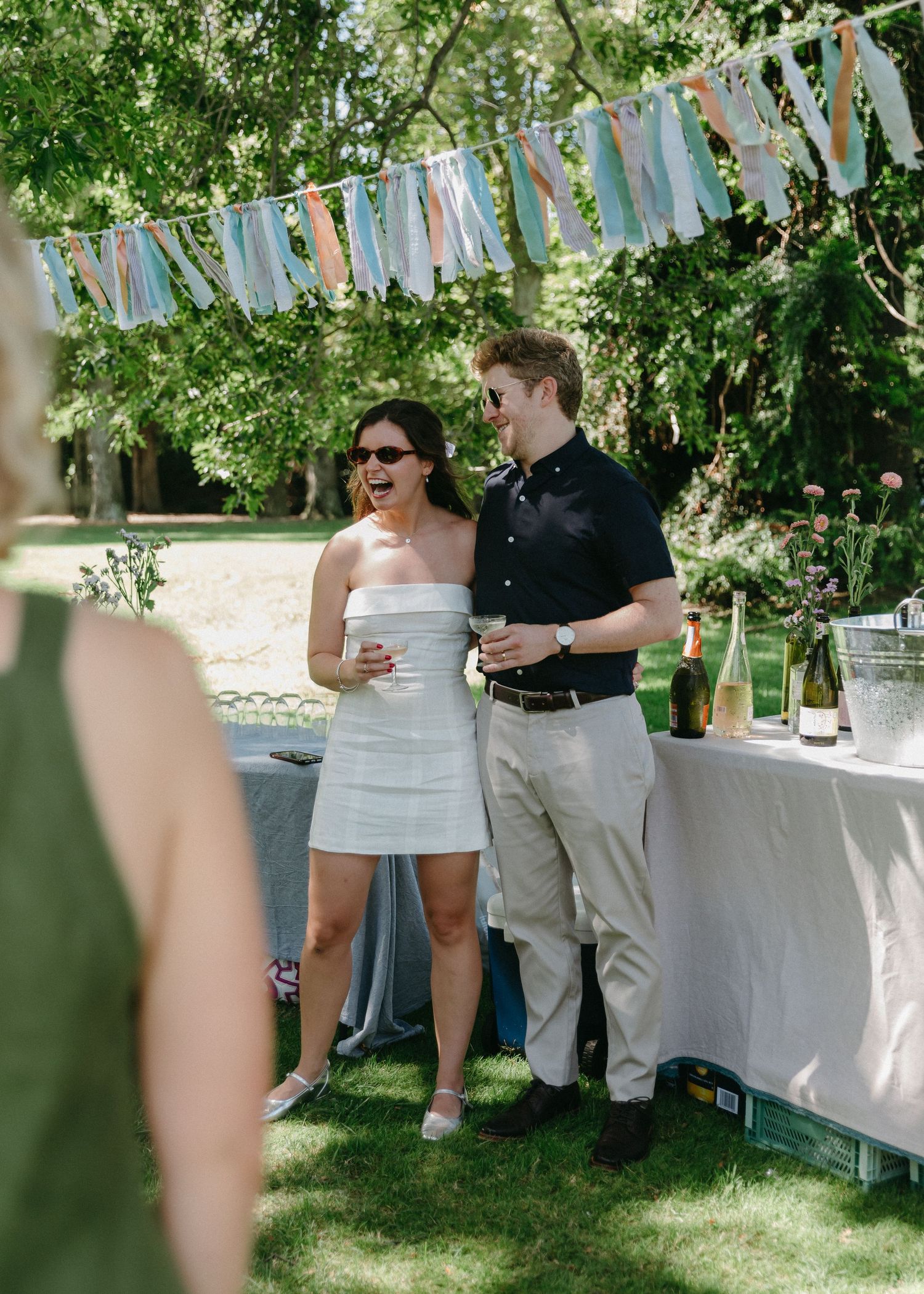 Newlywed couple laughs together at outdoor garden wedding reception under festive bunting.