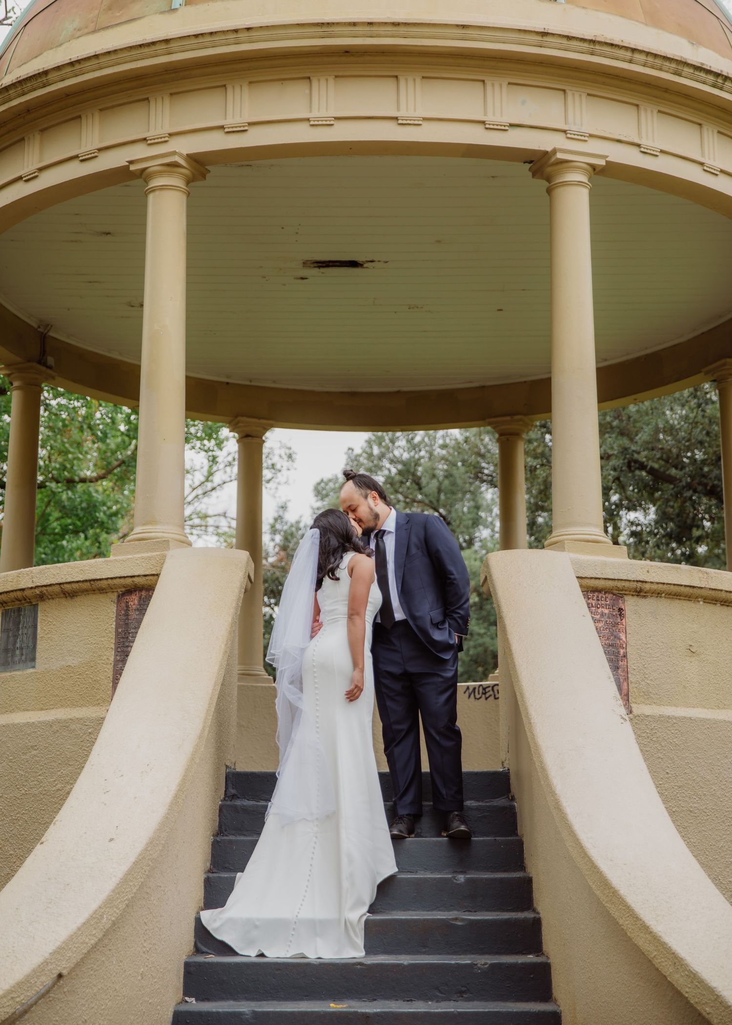 Bride and groom share a romantic kiss on the steps of an elegant rotunda gazebo.