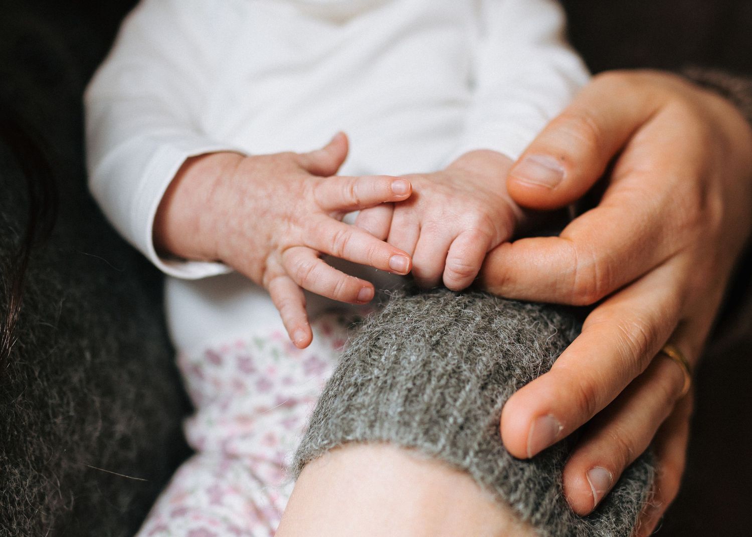 Newborn baby hand gently grasping an adult finger in a tender moment of connection.