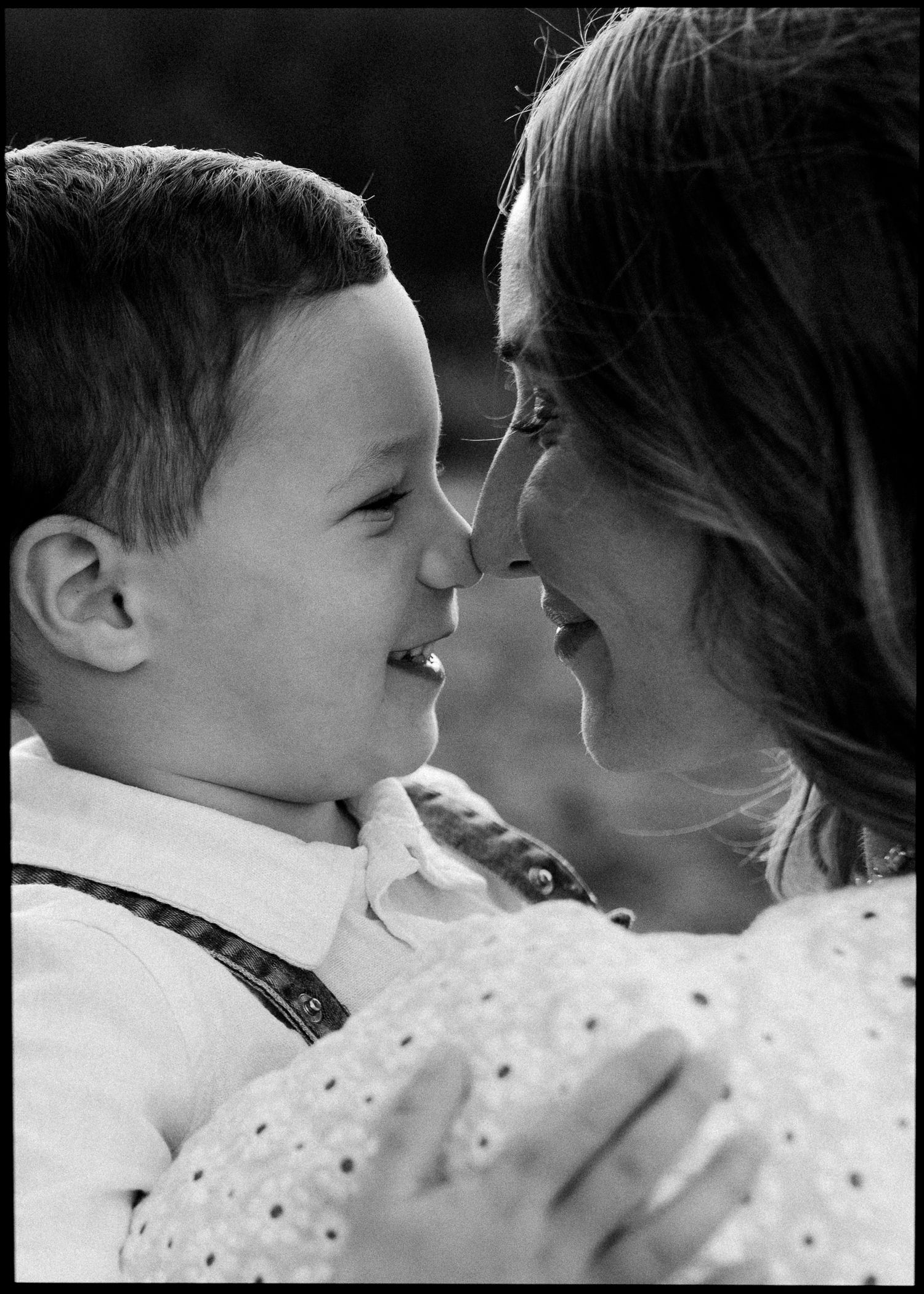 Black and white photo of a joyful boy and his mother sharing a nose-to-nose moment outdoors.