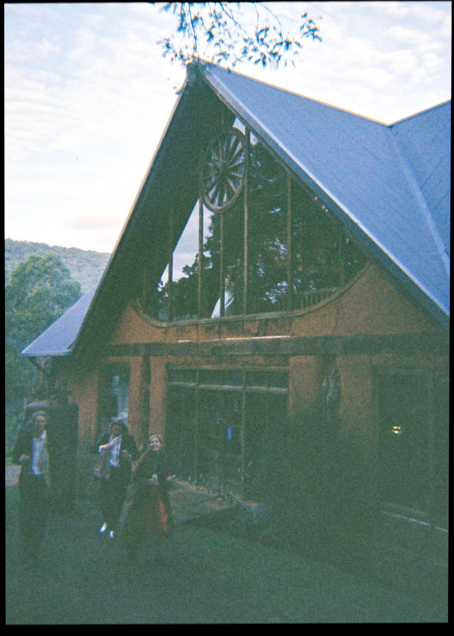 Rustic A-frame wedding venue with a wagon wheel window detail and guests arriving at dusk.
