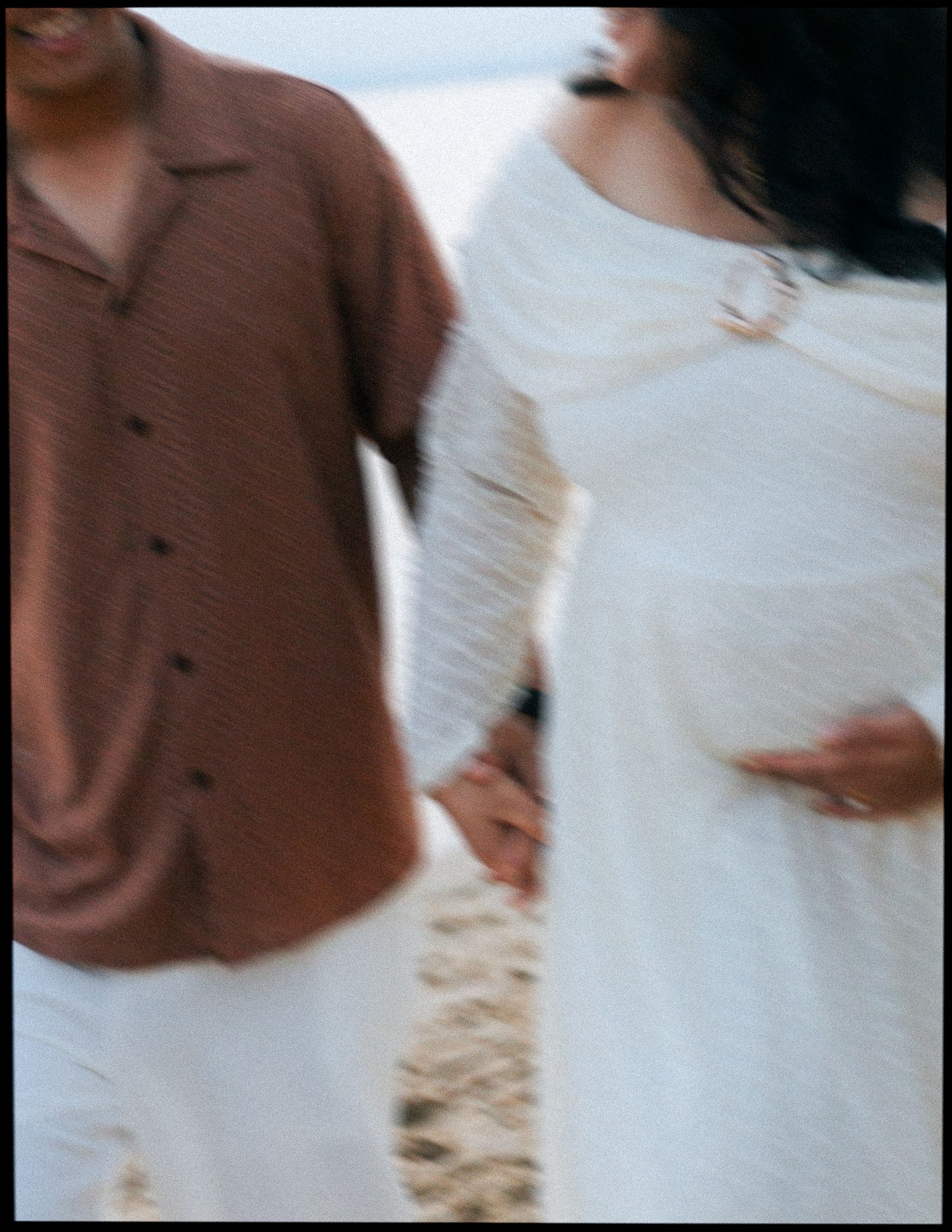 Close-up of pregnant couple holding hands on the beach in matching outfits.
