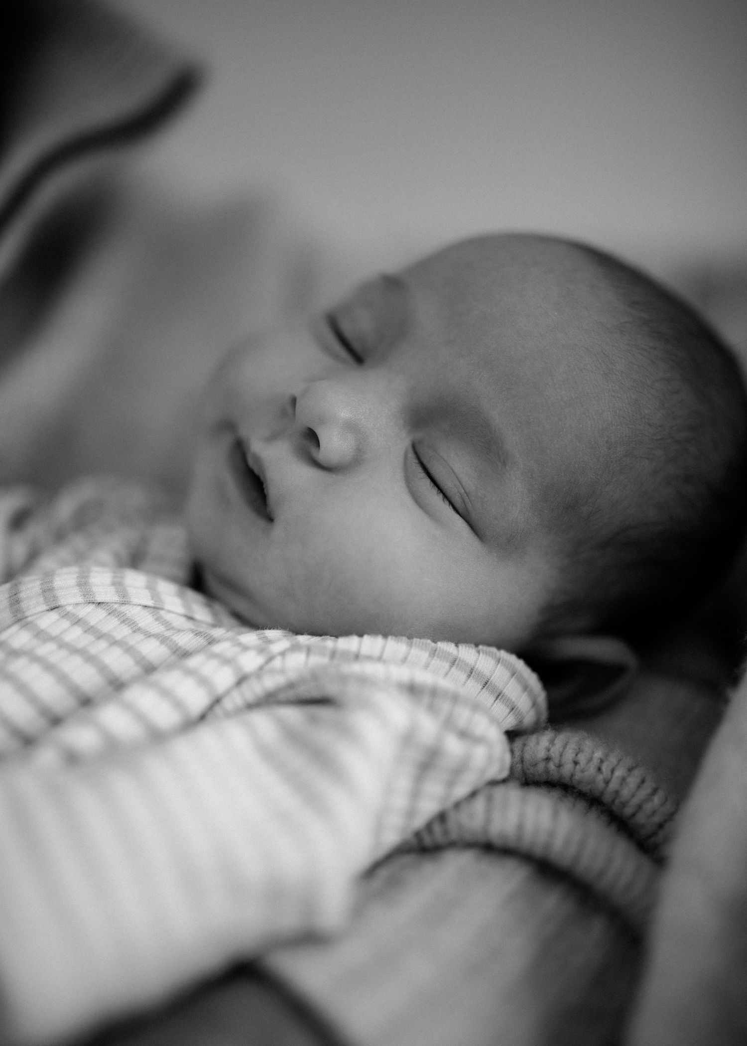 Black and white close-up portrait of serene sleeping newborn baby in soft striped clothing.
