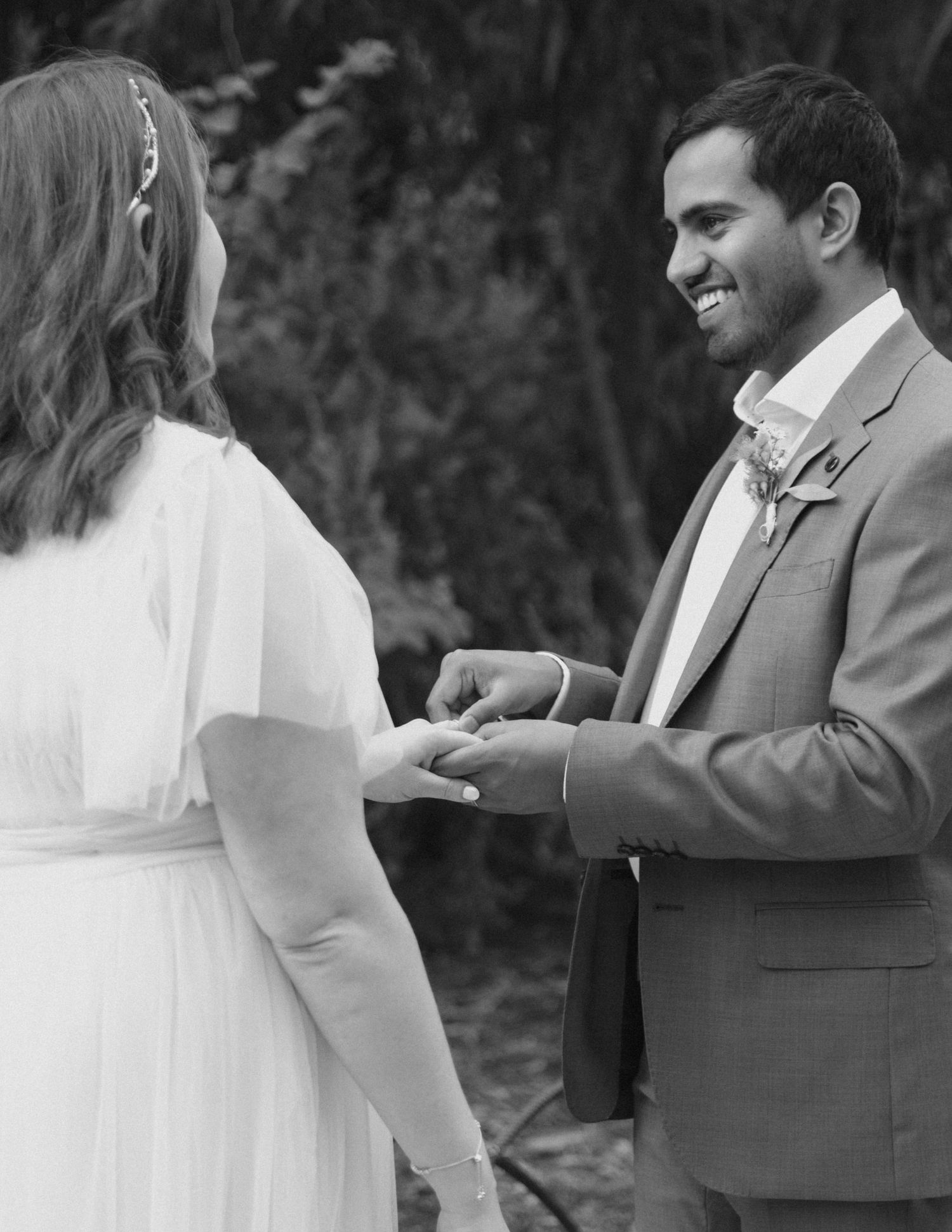 Groom places wedding ring on bride's finger during outdoor ceremony in black and white.