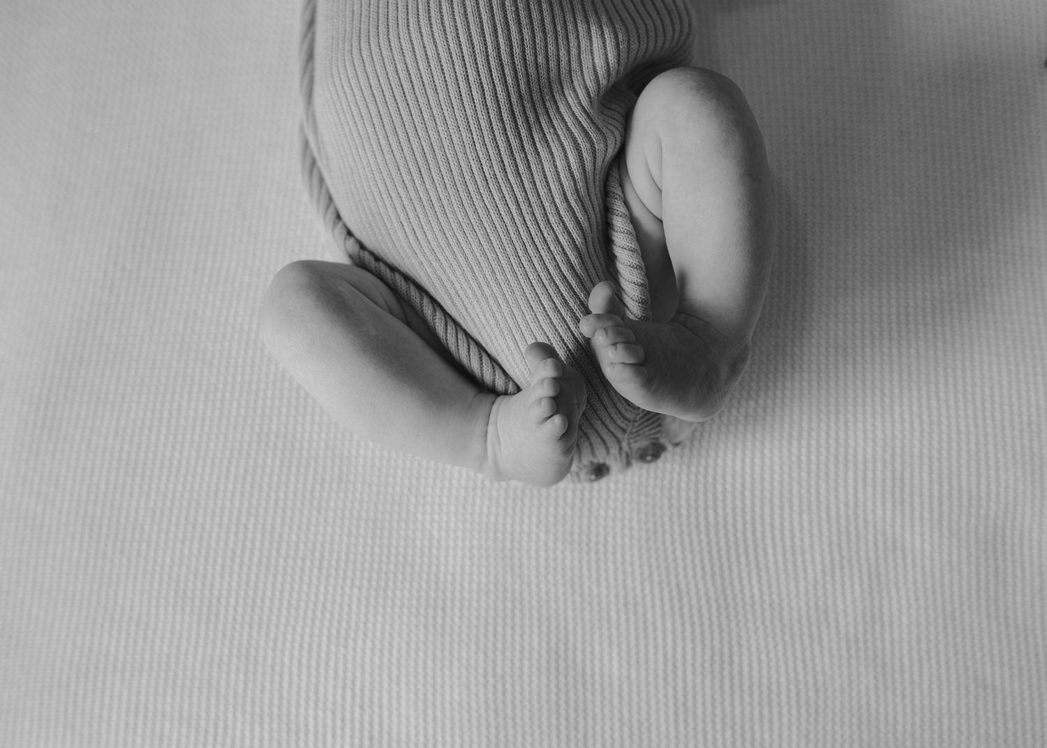 Black and white close-up of newborn baby feet in striped outfit on soft blanket.