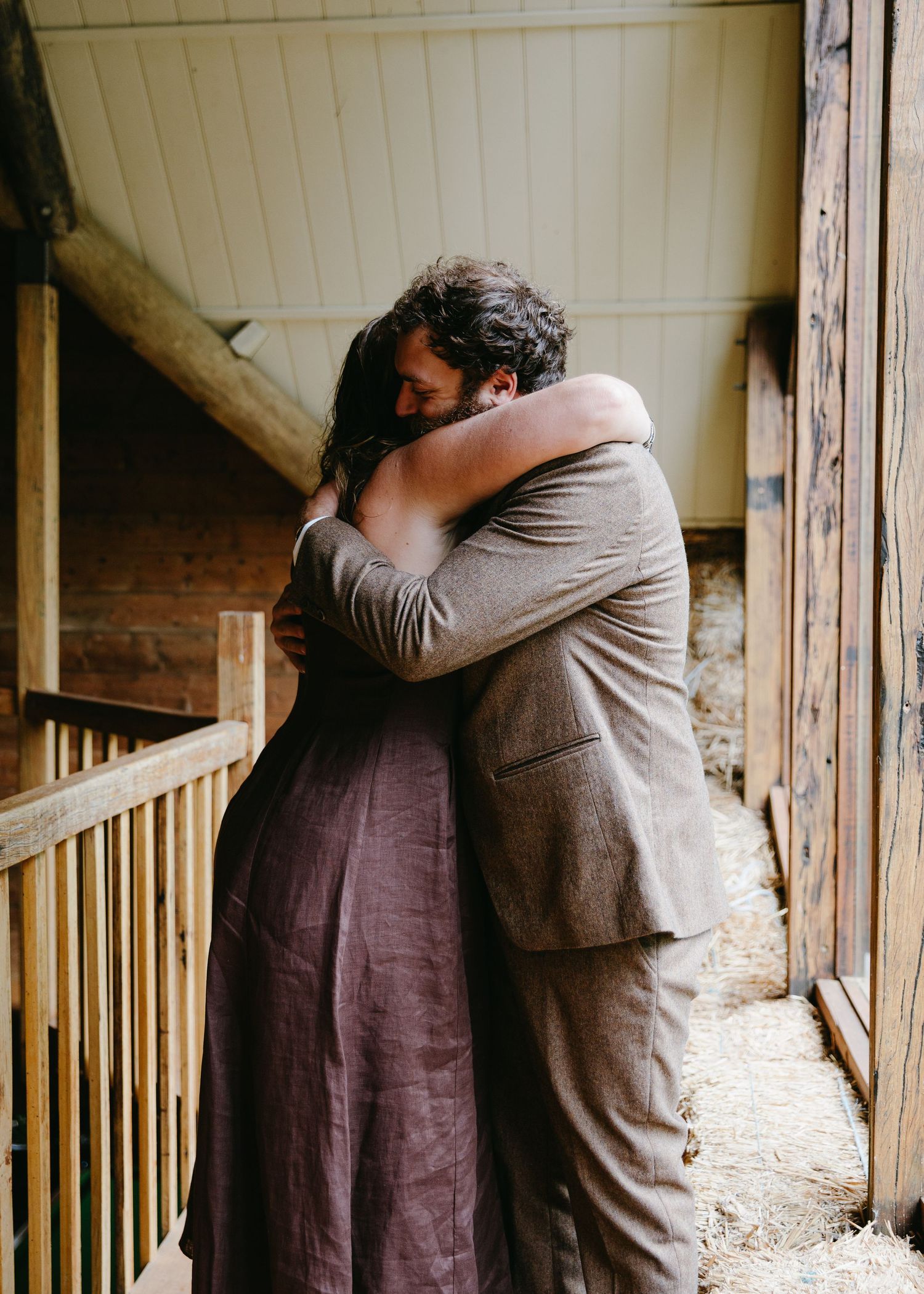 Couple sharing a tender embrace in a rustic barn hallway before their wedding ceremony.