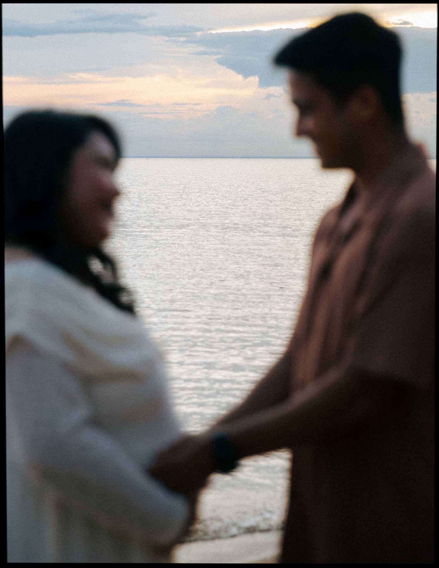 Blurred artistic photo of expecting couple holding hands with ocean backdrop.