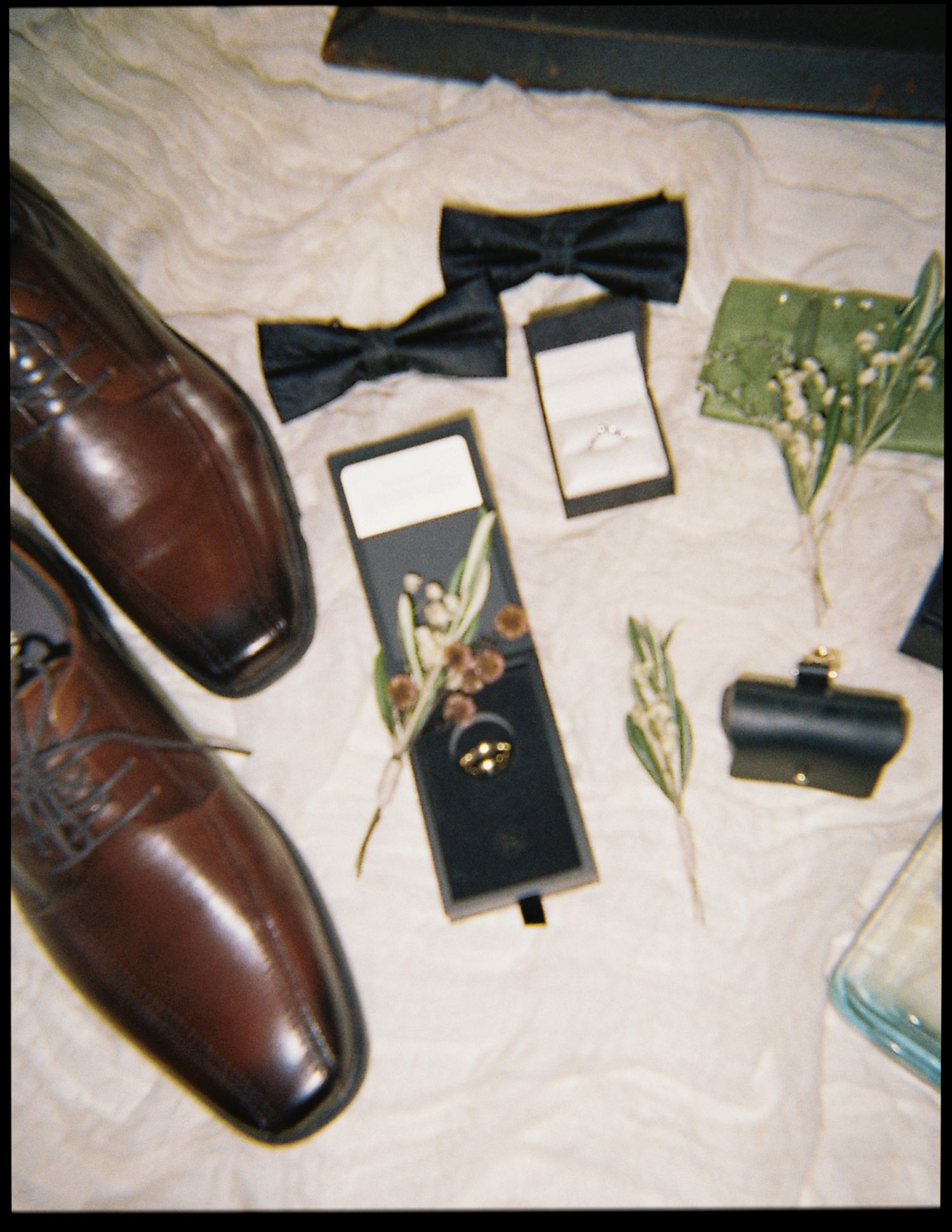 Wedding day groom details flatlay with brown oxford shoes, black bow tie, rings, and cufflinks.