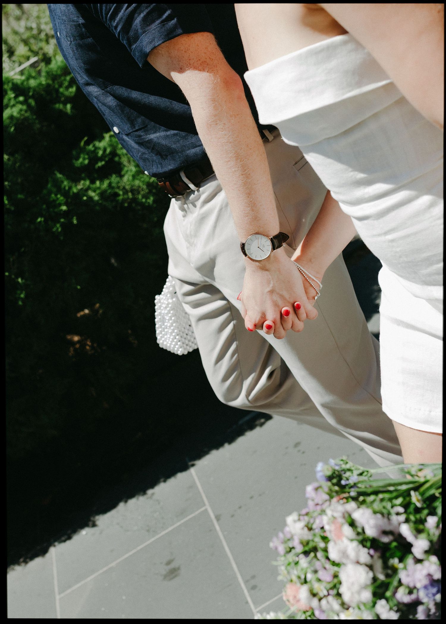 Close-up of a couple holding hands, bride wearing red nail polish and a delicate watch on her wrist.