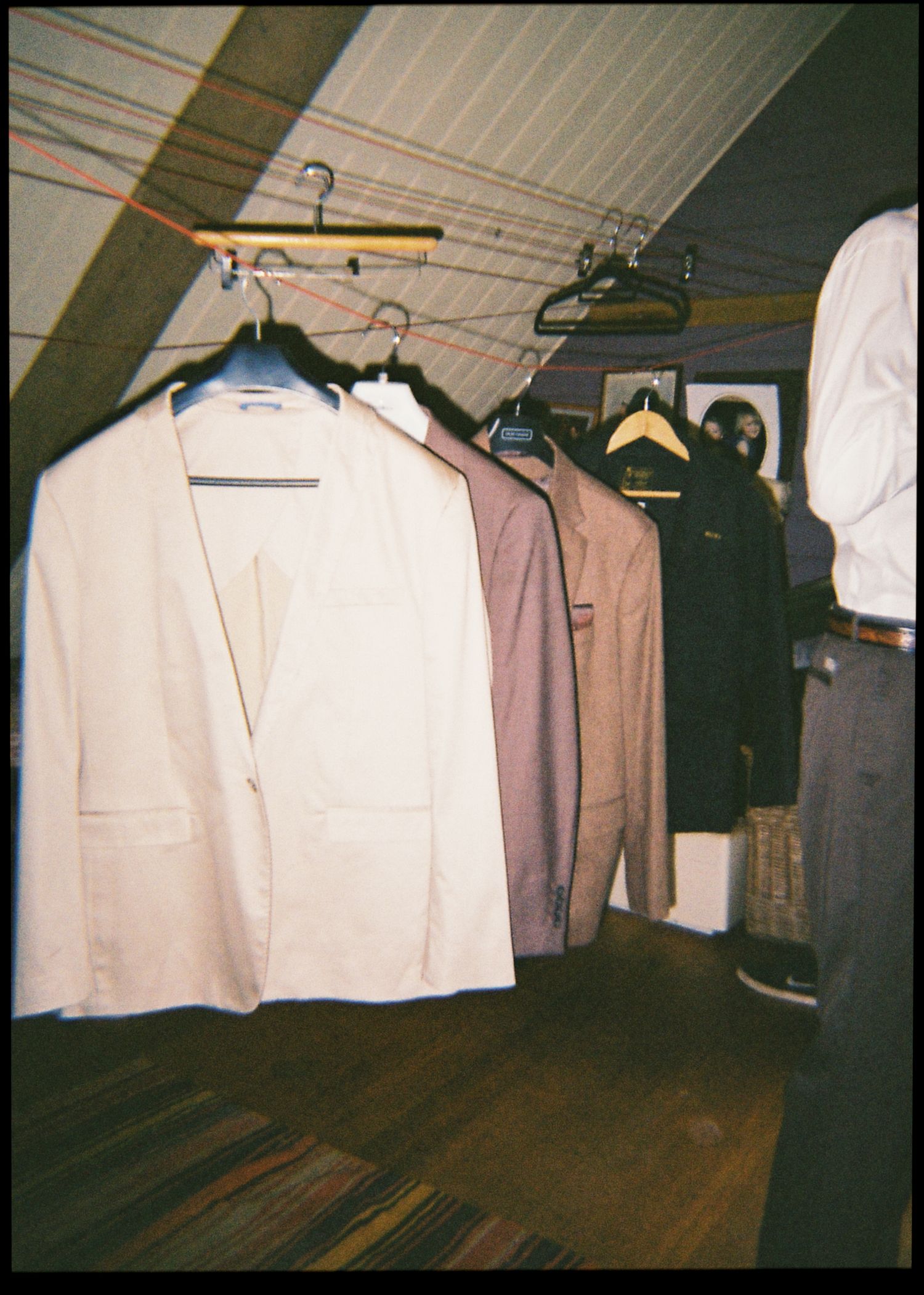 Collection of suits and jackets hanging on wooden hangers in a rustic attic space.