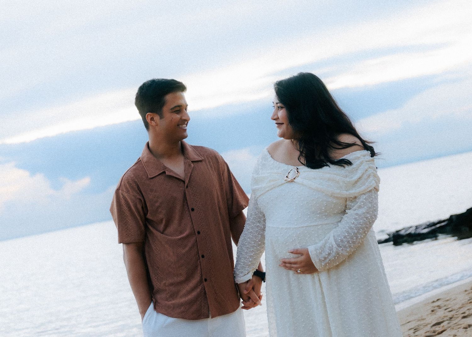 Happy expecting couple holding hands on the beach during maternity photoshoot.