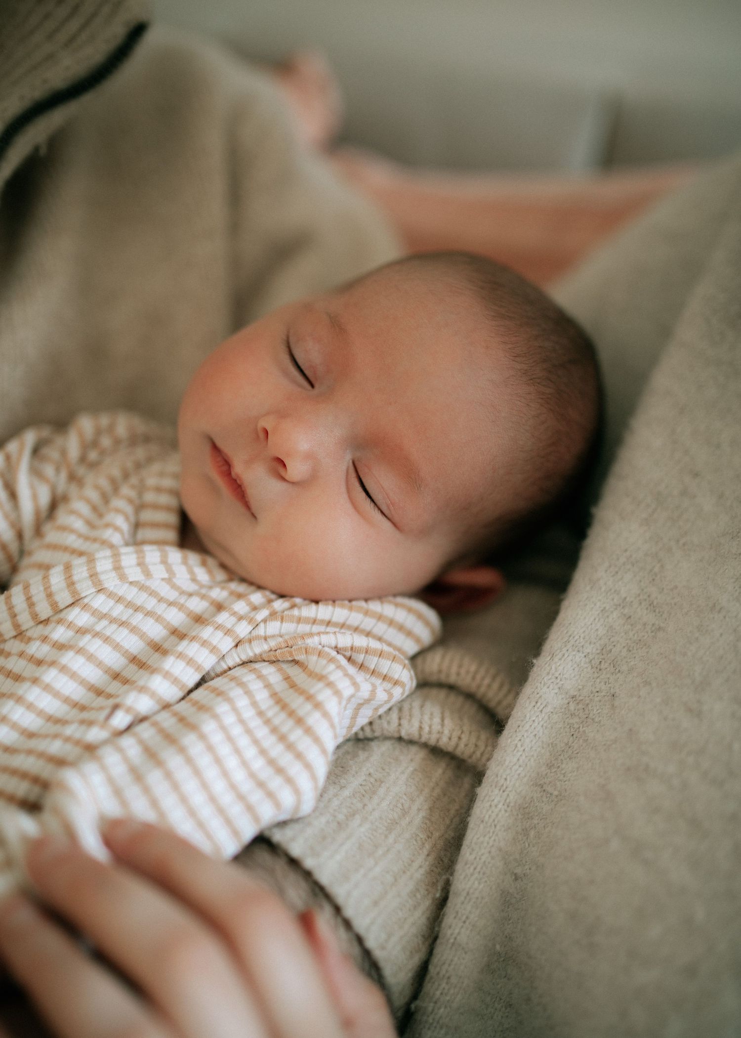 Sleeping newborn baby in striped onesie resting peacefully in parents arms on cozy blanket.