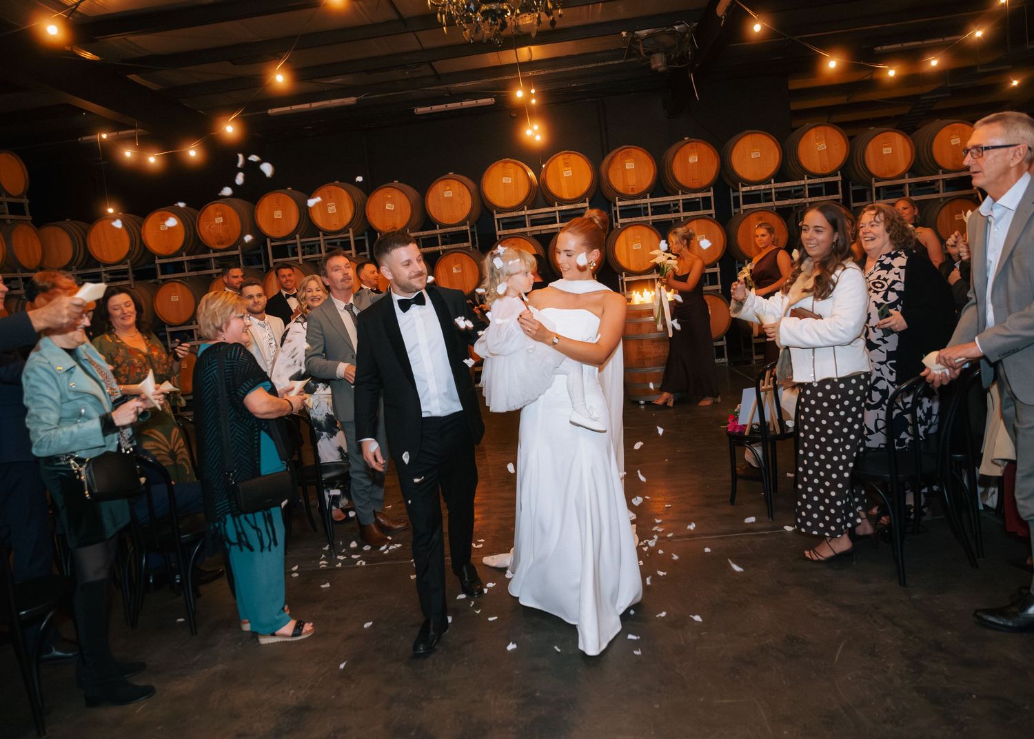 Bride and groom walk through petal toss at winery wedding reception with barrel wall backdrop.