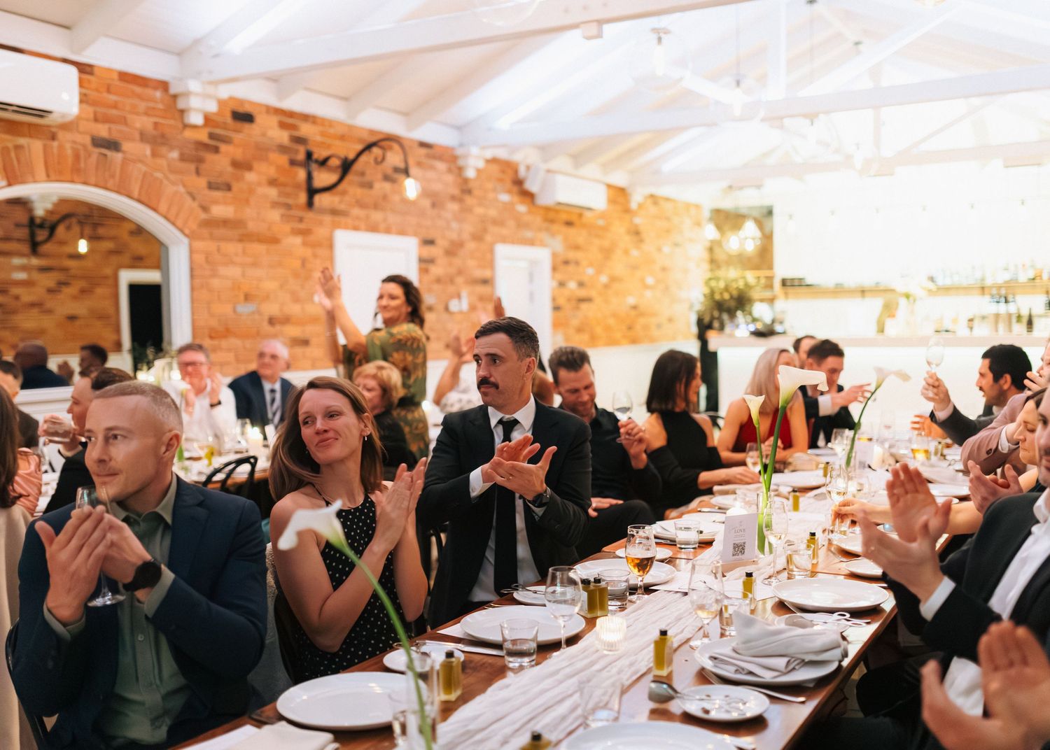 Wedding guests clapping and celebrating at outdoor reception under white marquee tent.