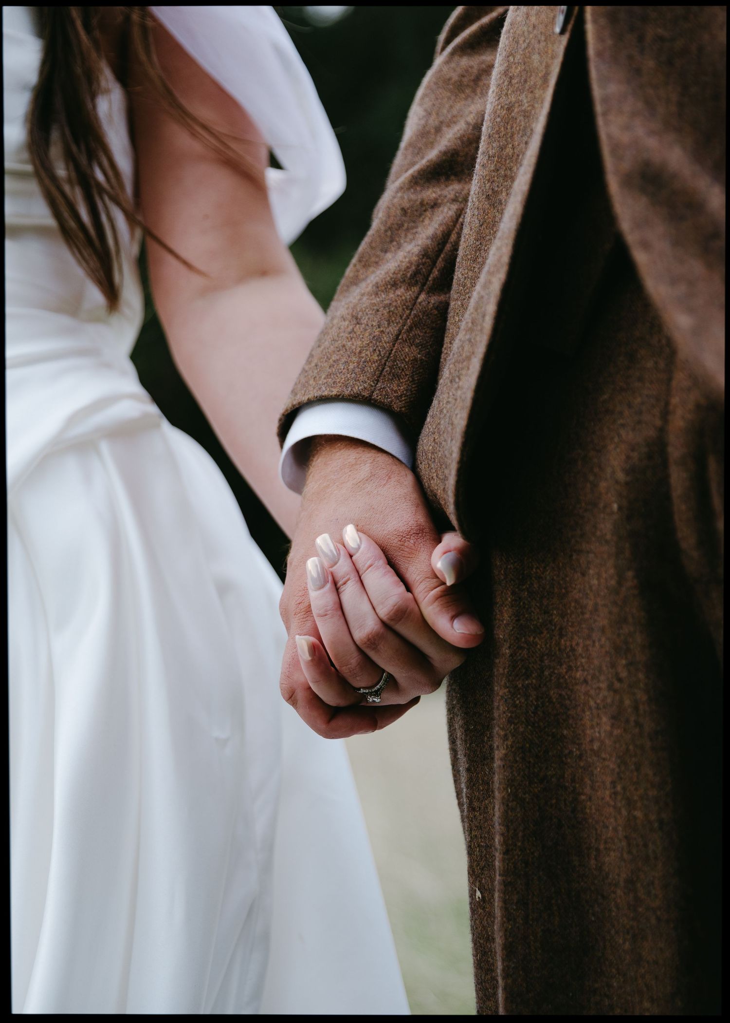 Close-up of bride and groom holding hands, bride wearing a wedding ring and white gown.