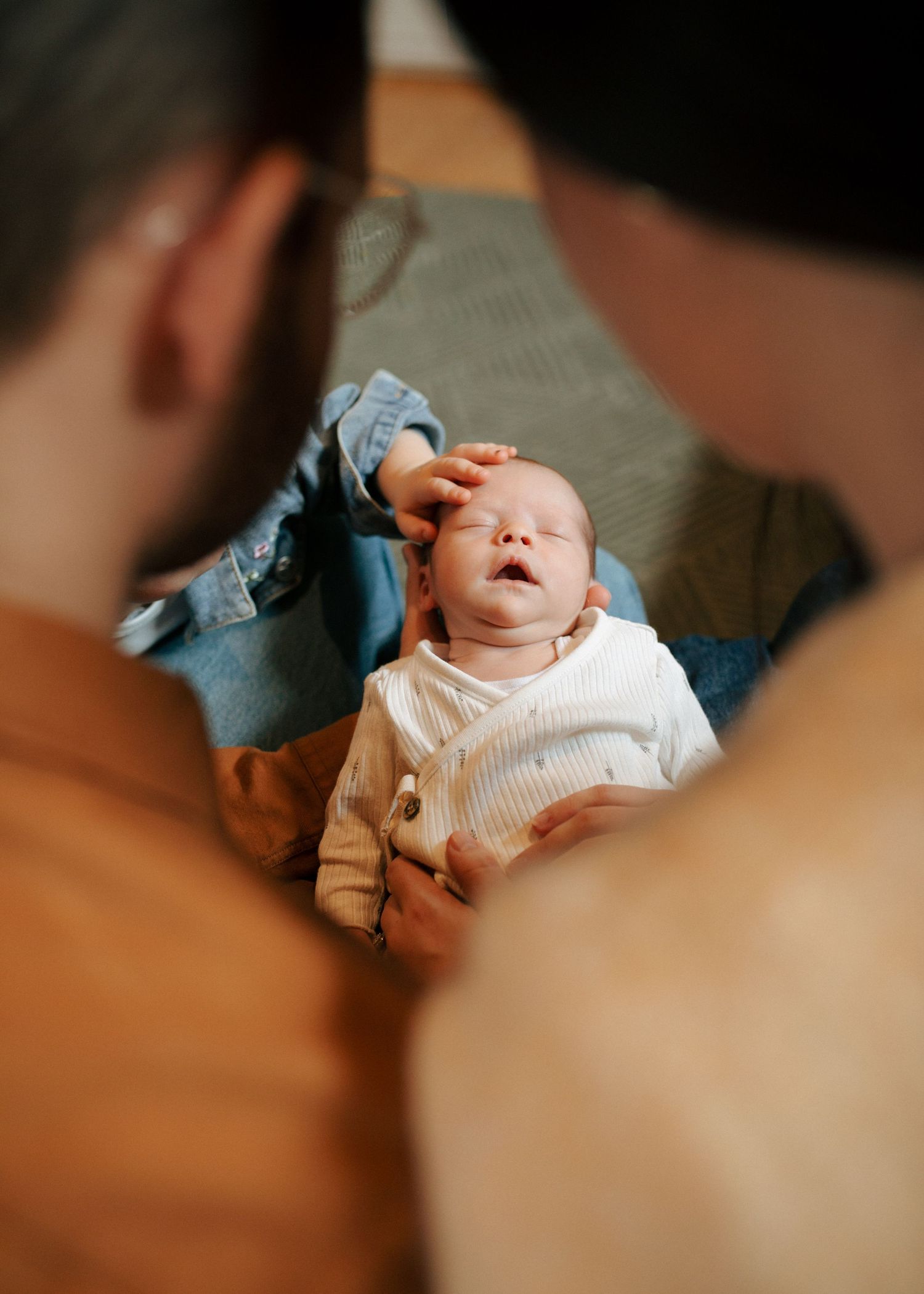 Two parents lovingly tend to their newborn baby lying on a soft surface, gently touching the infant's head.jpg