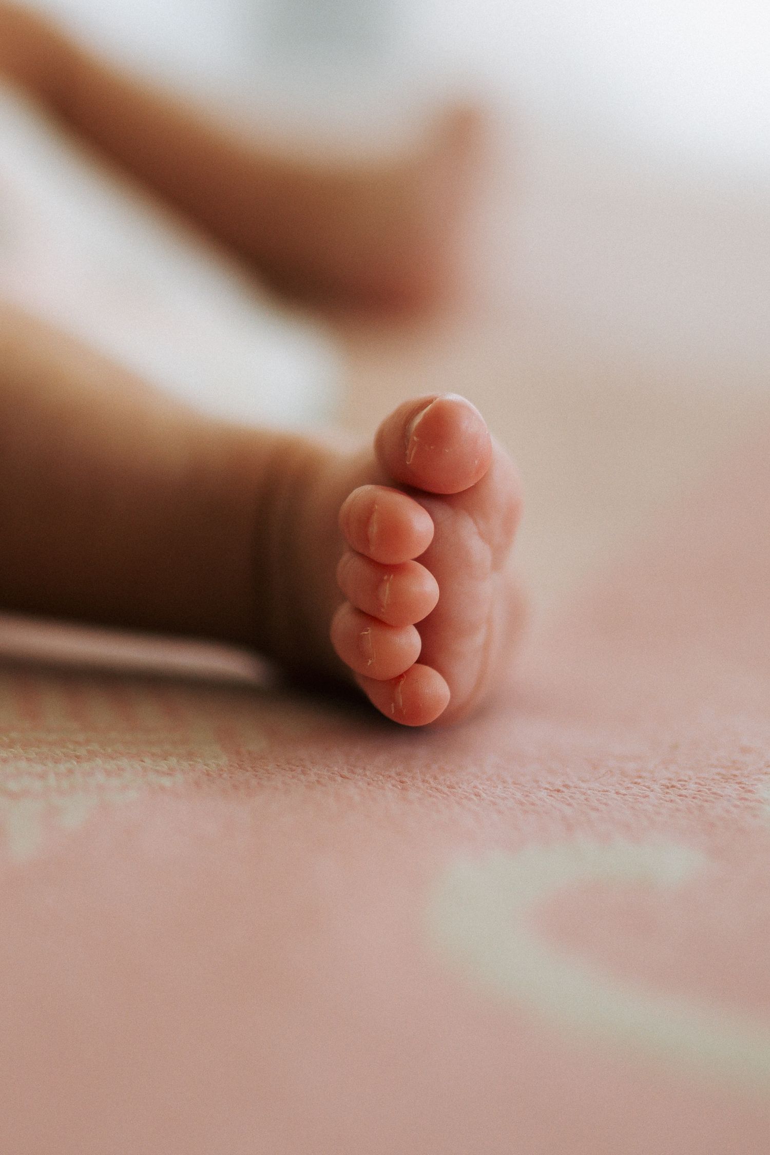 Close-up of a newborn babys tiny feet and toes on a soft pink blanket.