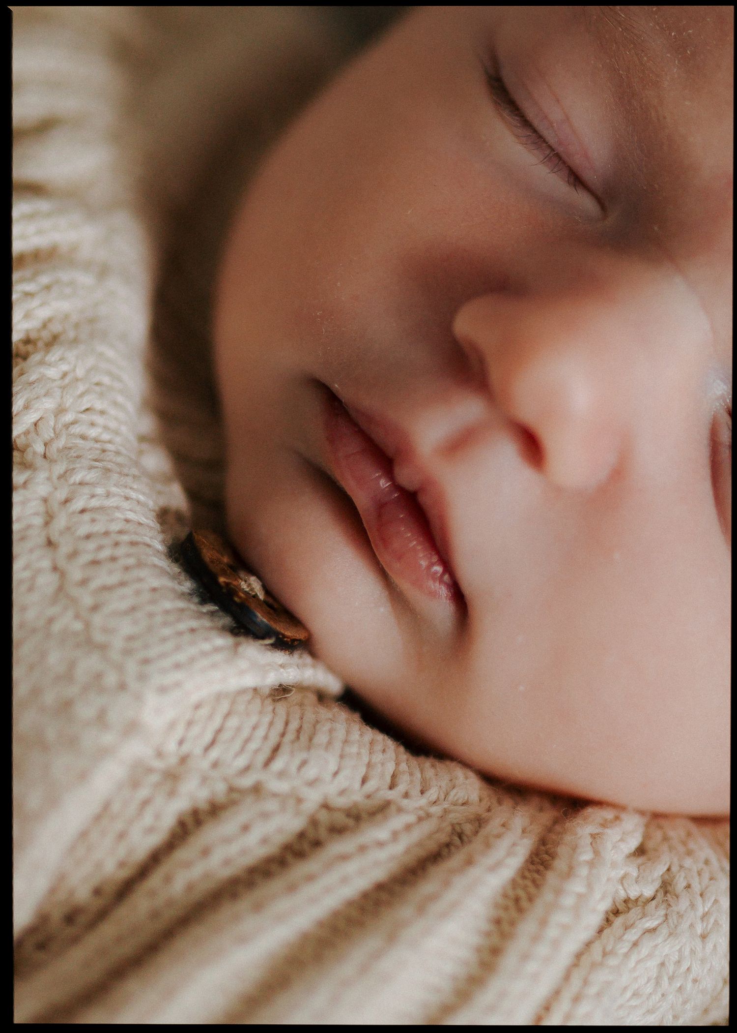 Peaceful sleeping newborn baby wrapped in soft cream knit blanket closeup.