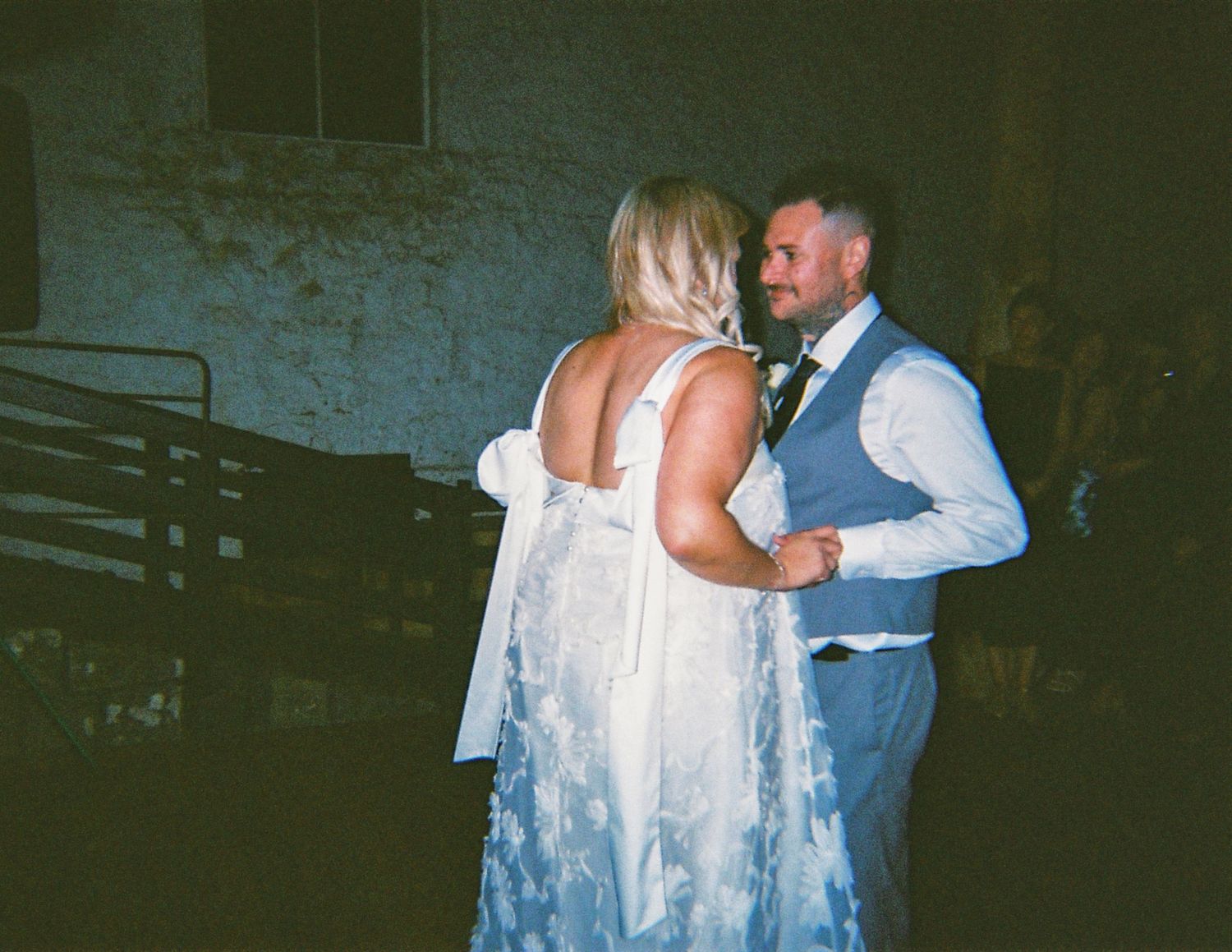 Bride in lace backless gown and groom in vest sharing a romantic first dance at their wedding reception.