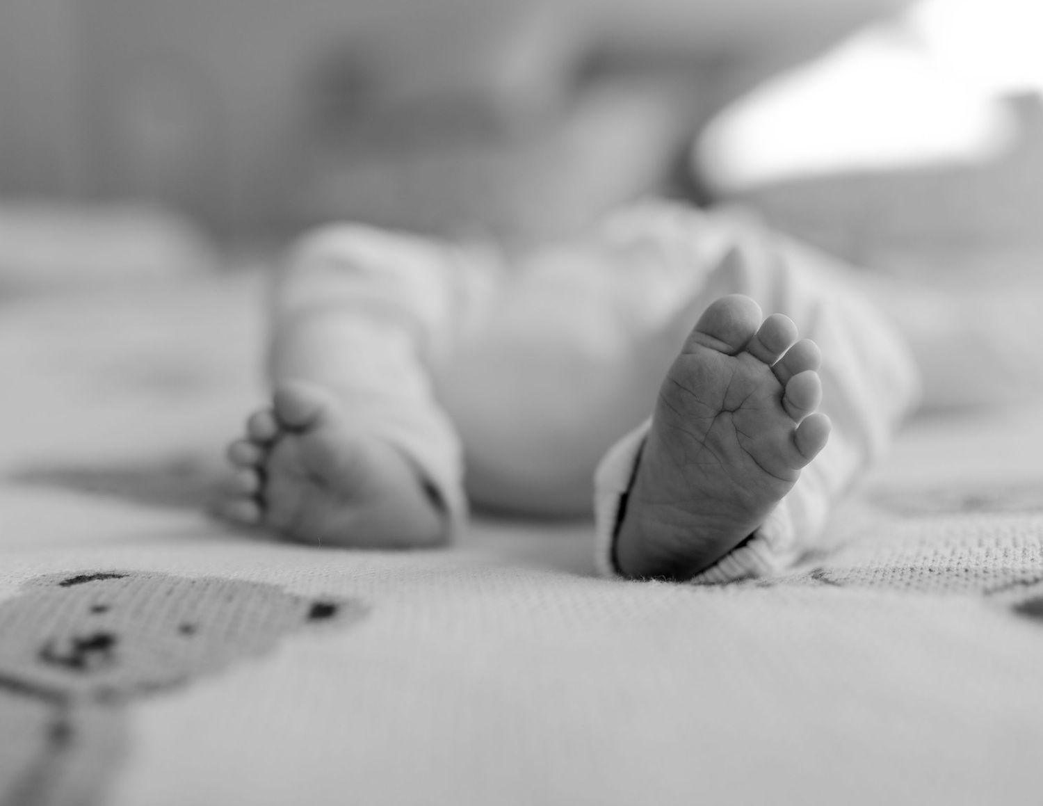 Close-up black and white photo of newborn baby feet on a soft blanket.