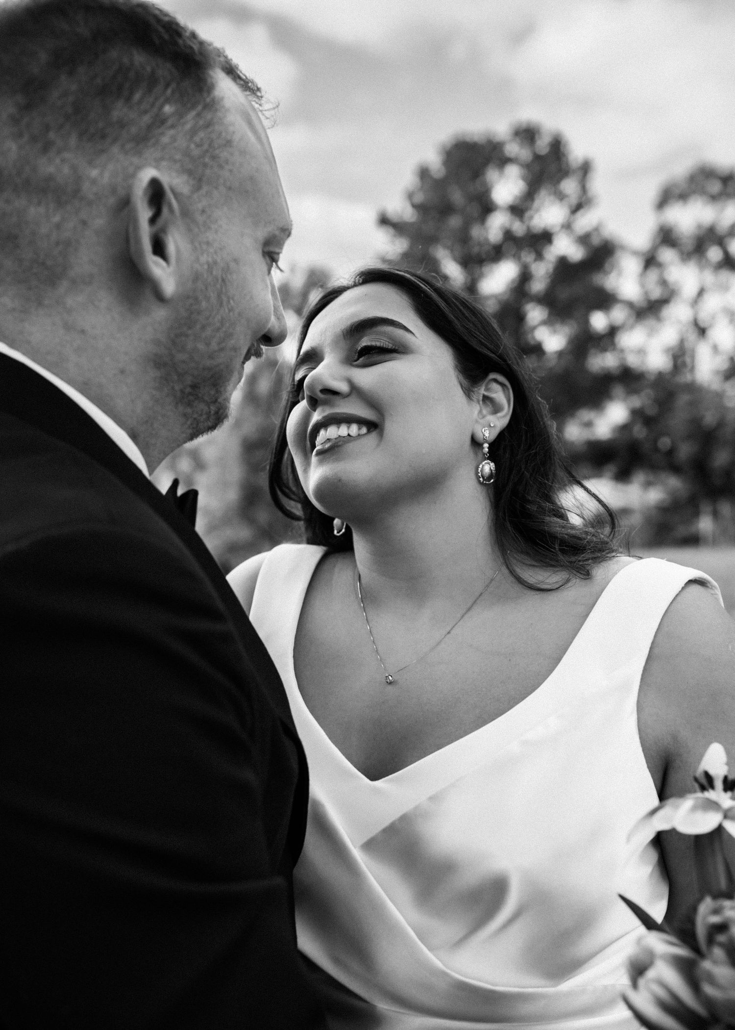 Black and white close-up of smiling bride gazing at groom during outdoor wedding ceremony.