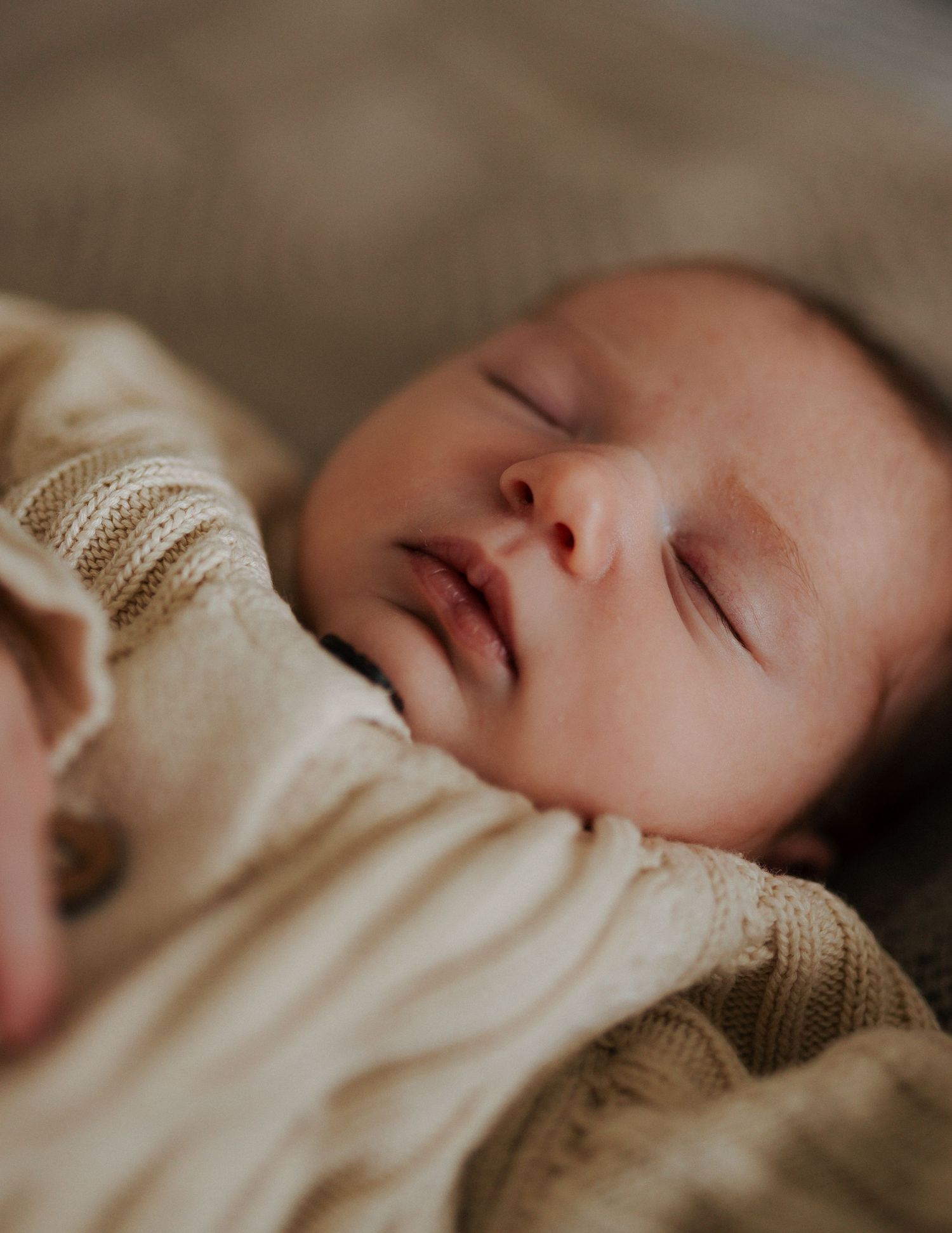 A peaceful newborn baby sleeping soundly in a cream knit outfit, with soft natural lighting.