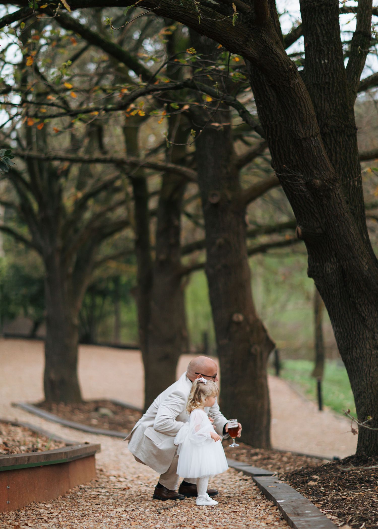 Older gentleman crouching to interact with flower girl in park.