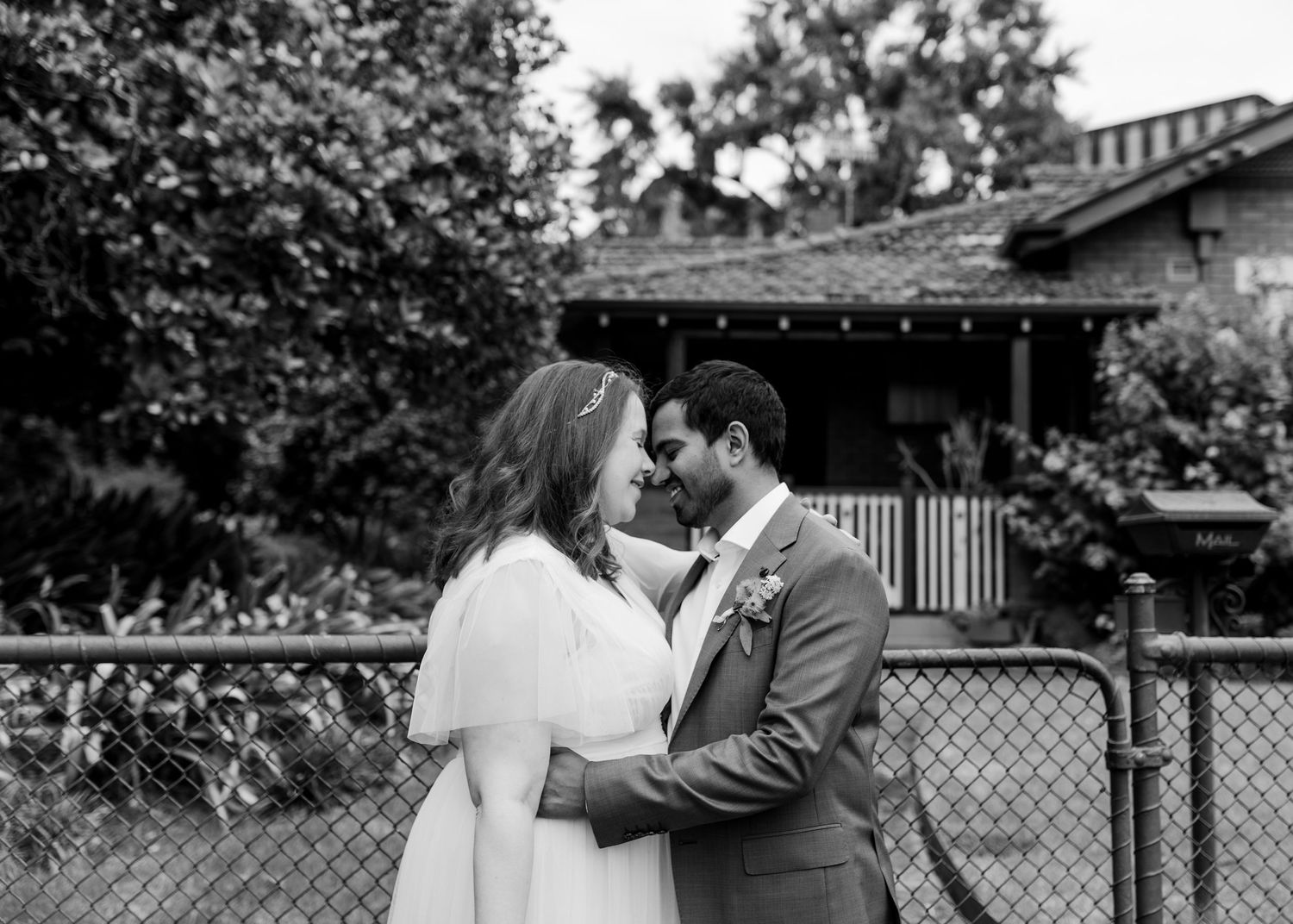 Black and white photo of bride and groom sharing an intimate moment, nearly kissing outdoors.