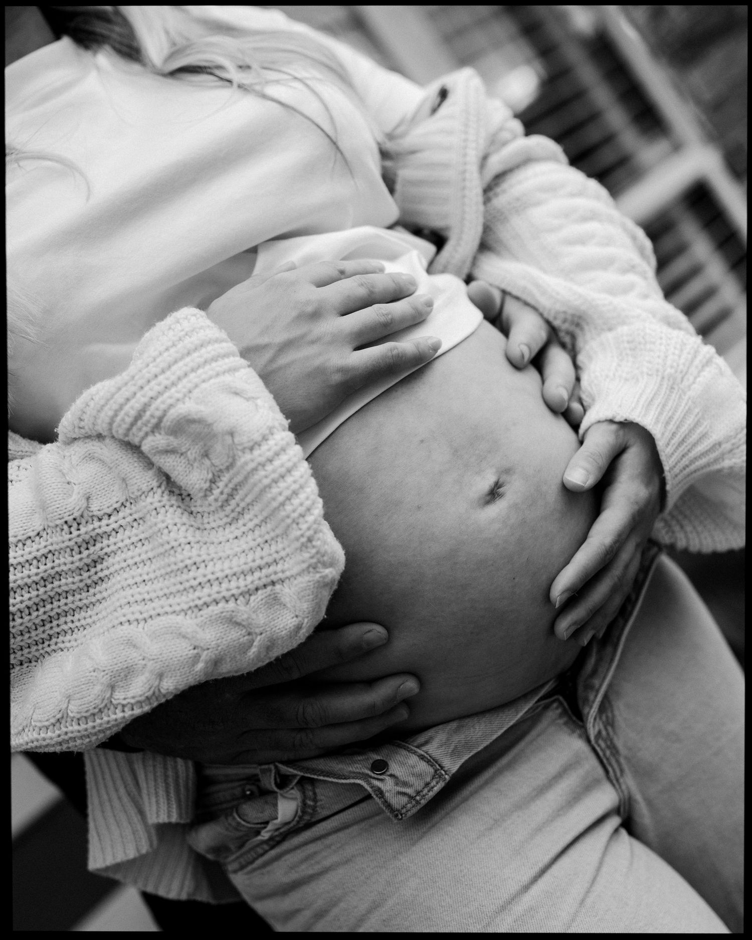 Black and white close-up of couple's hands tenderly cradling pregnant belly.
