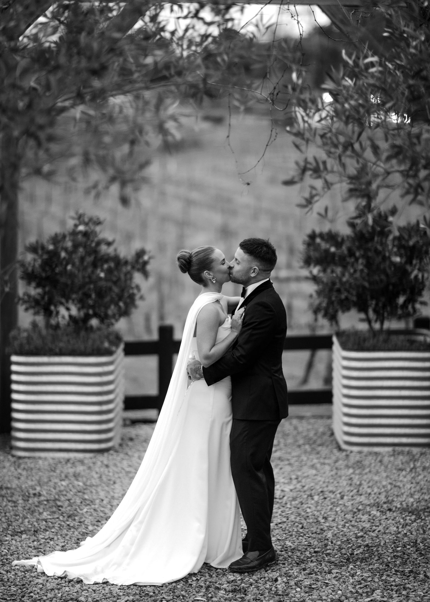 Black and white photo of bride and groom sharing a kiss in a garden setting on their wedding day.