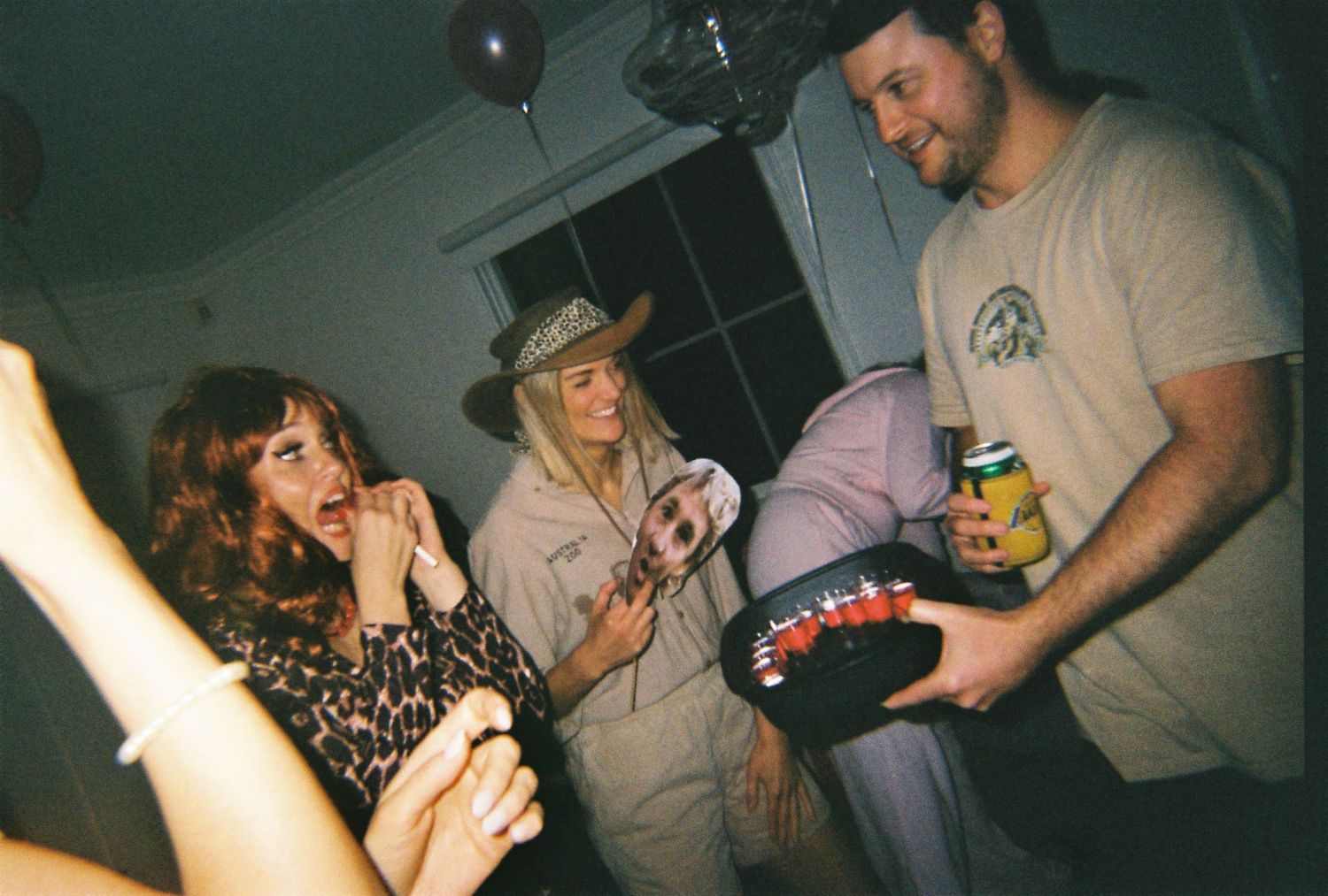 Three friends in Halloween costumes, including a cowboy hat, laugh and chat at an indoor party.