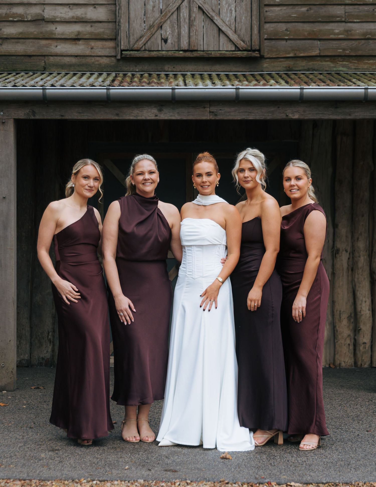 Bride in white halter gown surrounded by four bridesmaids in burgundy satin dresses.