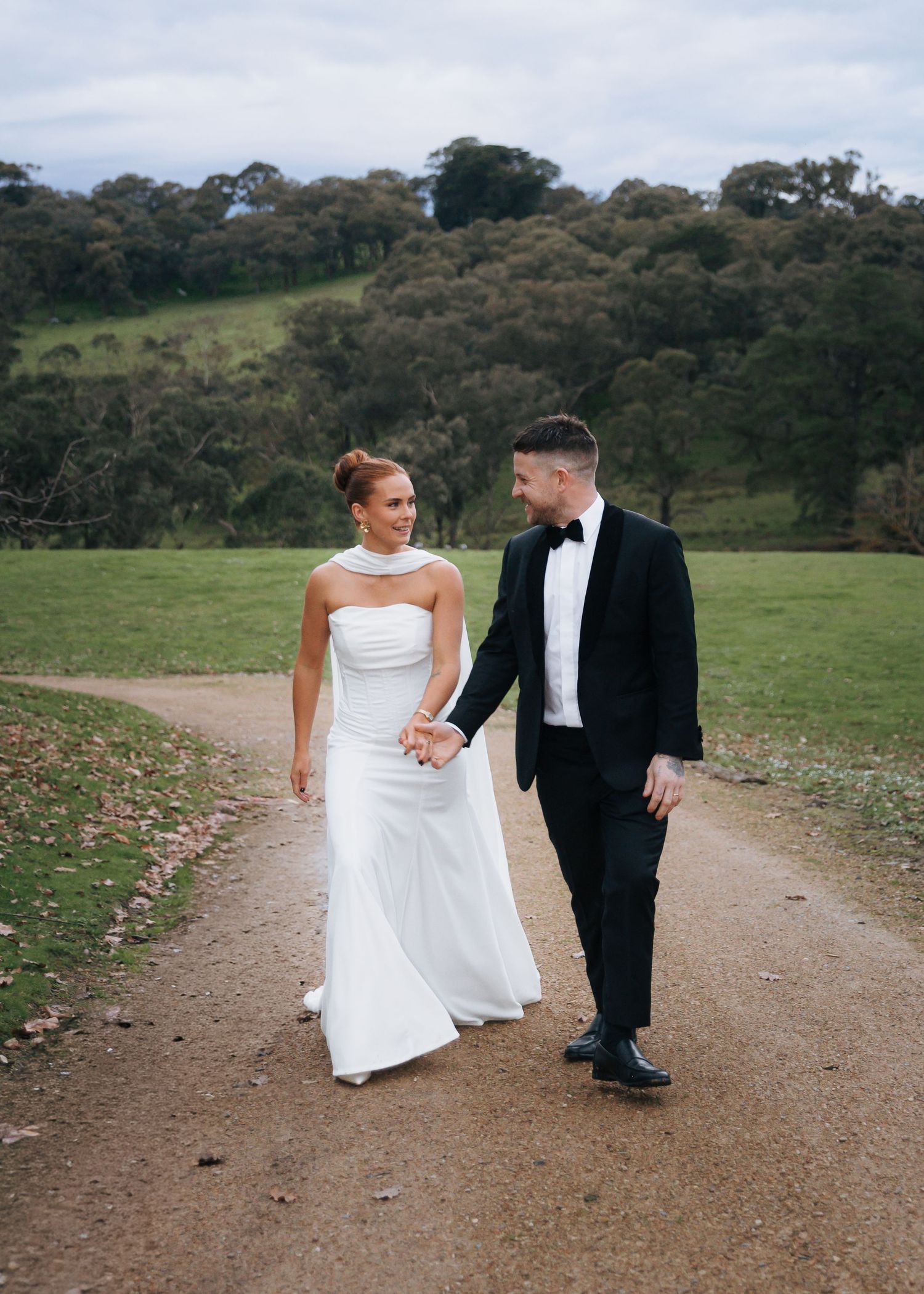Bride and groom walk hand in hand along scenic garden path on wedding day.