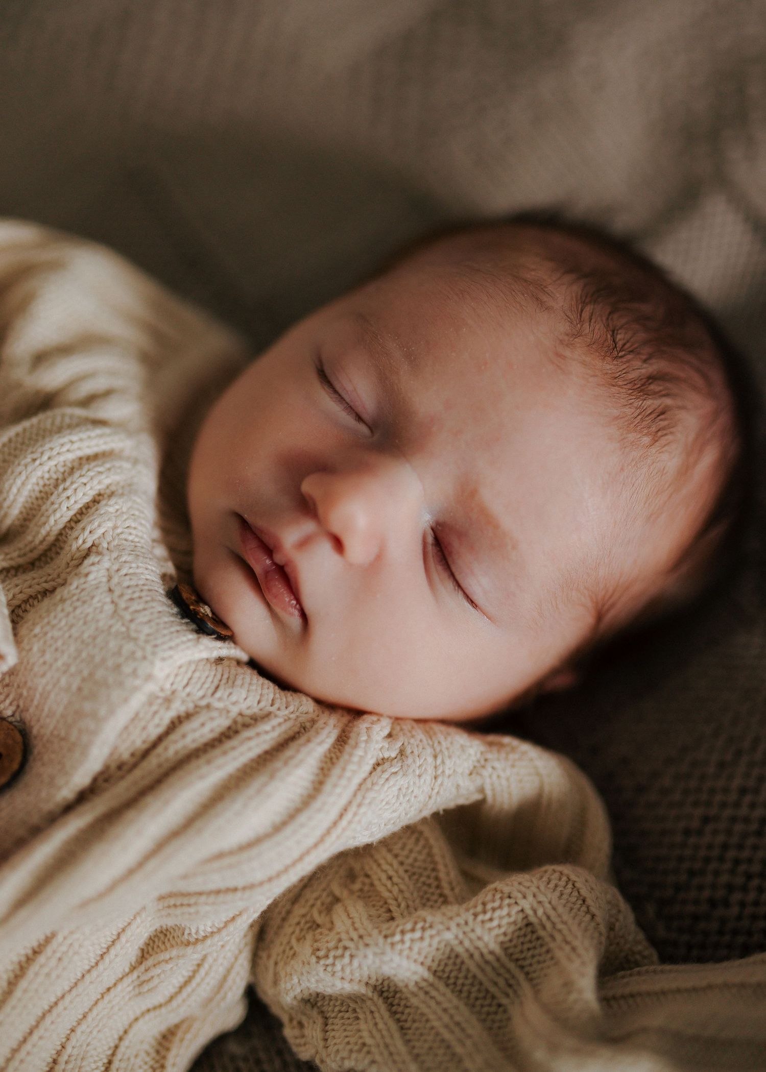 Sleeping newborn baby in cream knit onesie resting peacefully on a soft blanket.