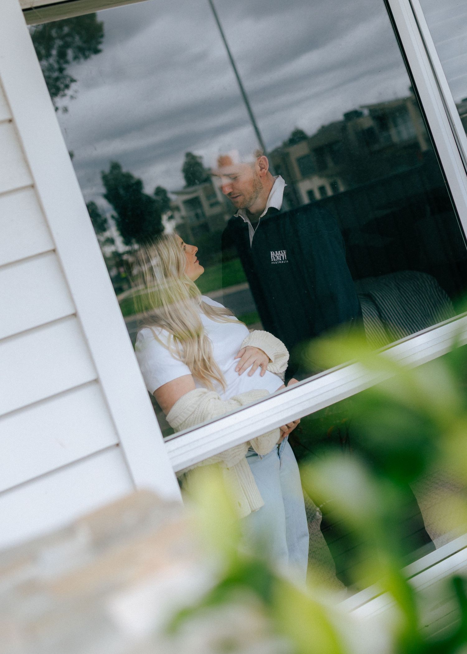 Couple sharing a tender moment photographed through a window reflection on a cloudy day.