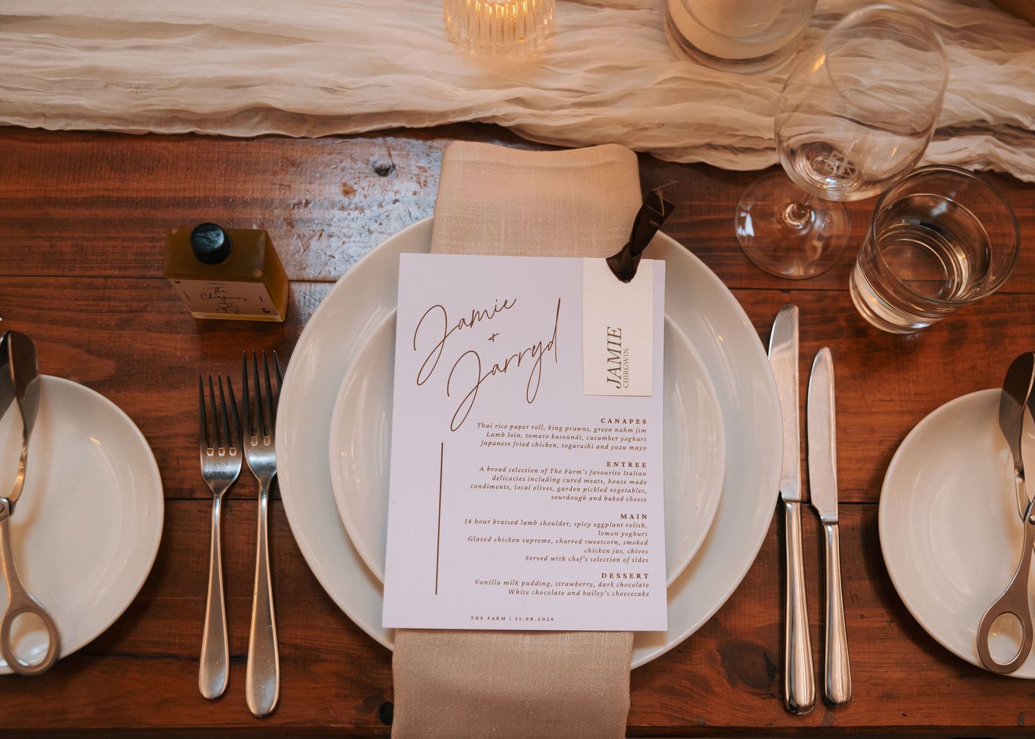 Elegant wedding place setting with calligraphy menu card, gold cutlery, white plates on rustic wood table.